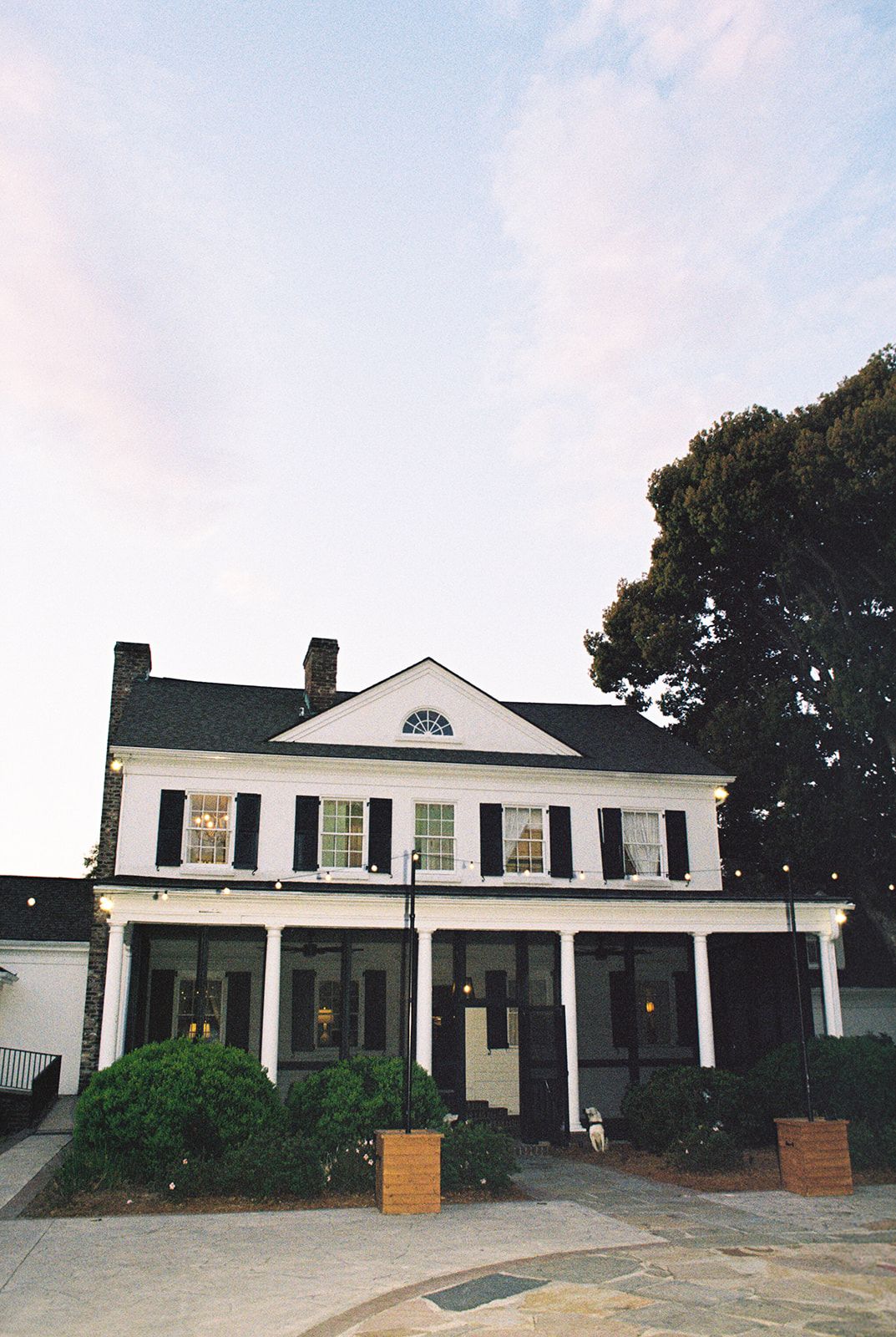A white colonial-style house with black shutters and multiple large columns stretches across the panoramic view.