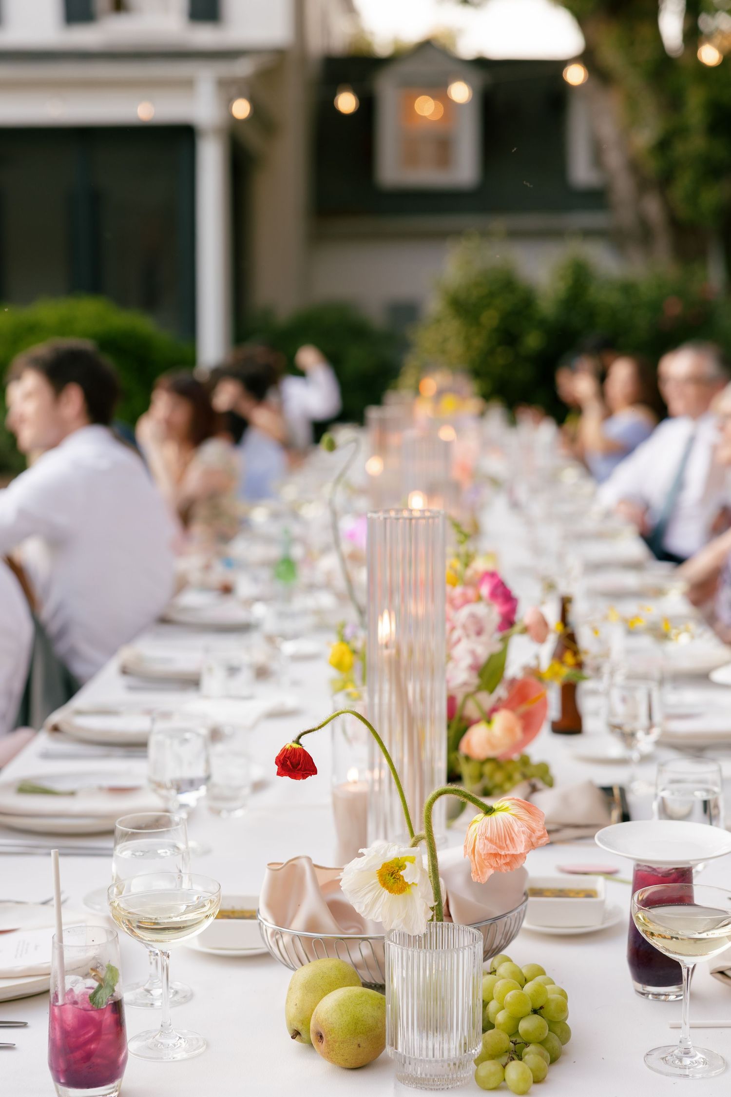 Elegant outdoor wedding reception table setting with floral centerpieces, candles, fresh fruit and wine glasses at sunset.