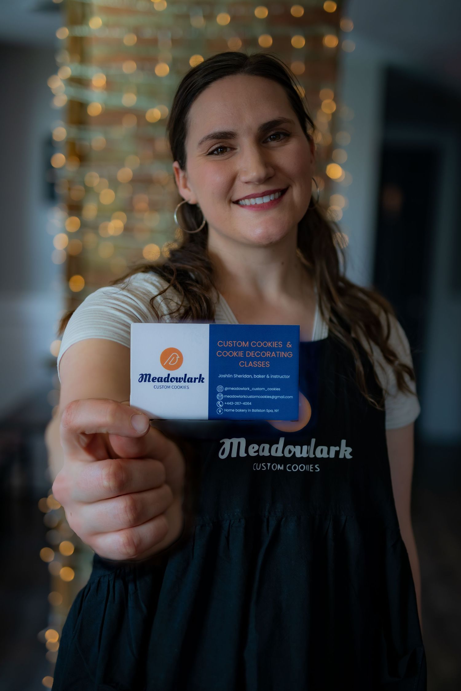 Someone showing a Meadowlark business card while wearing a dark apron, with twinkle lights glowing in the background.