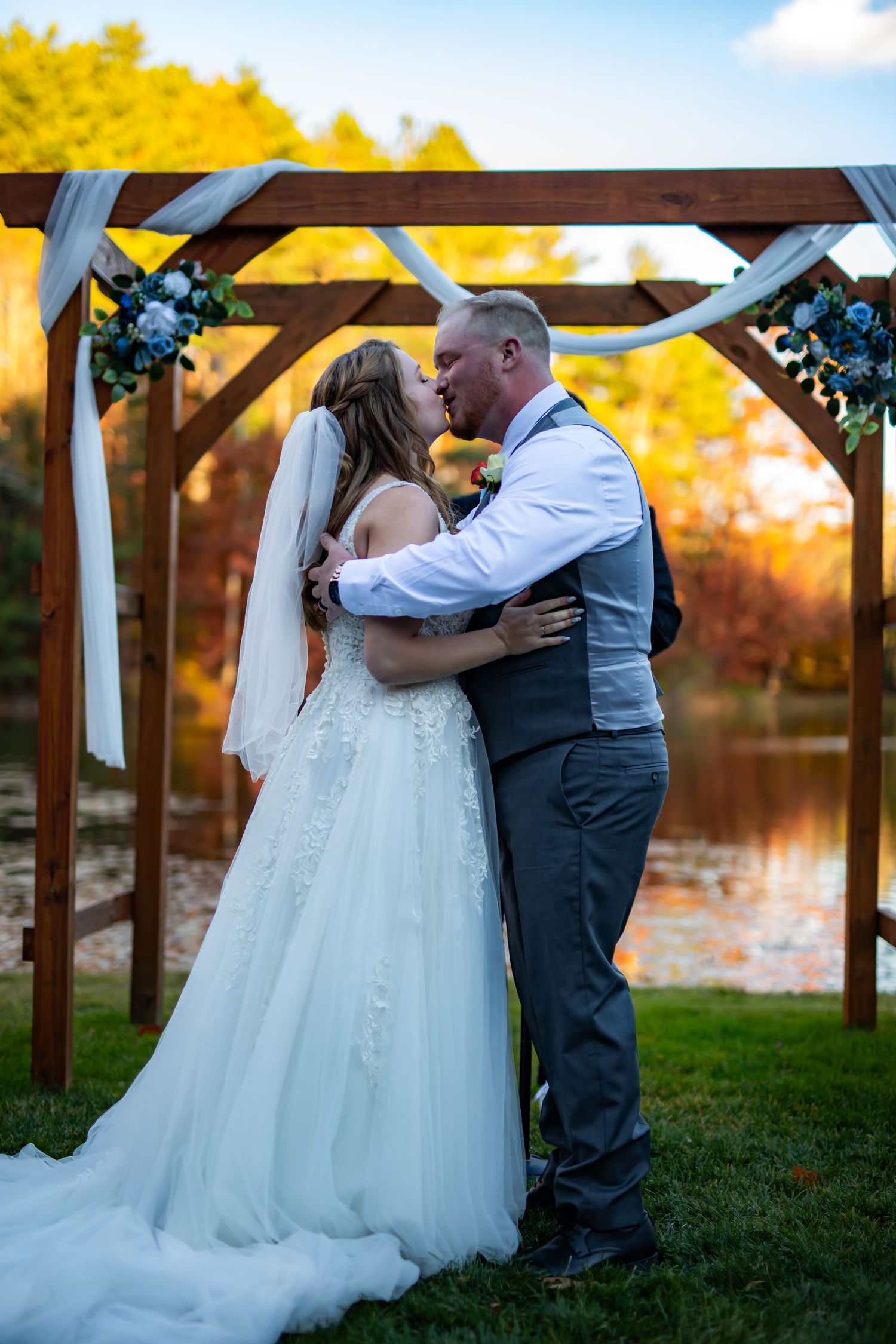 Romantic moment under wooden arch decorated with flowers by waterfront at sunset.