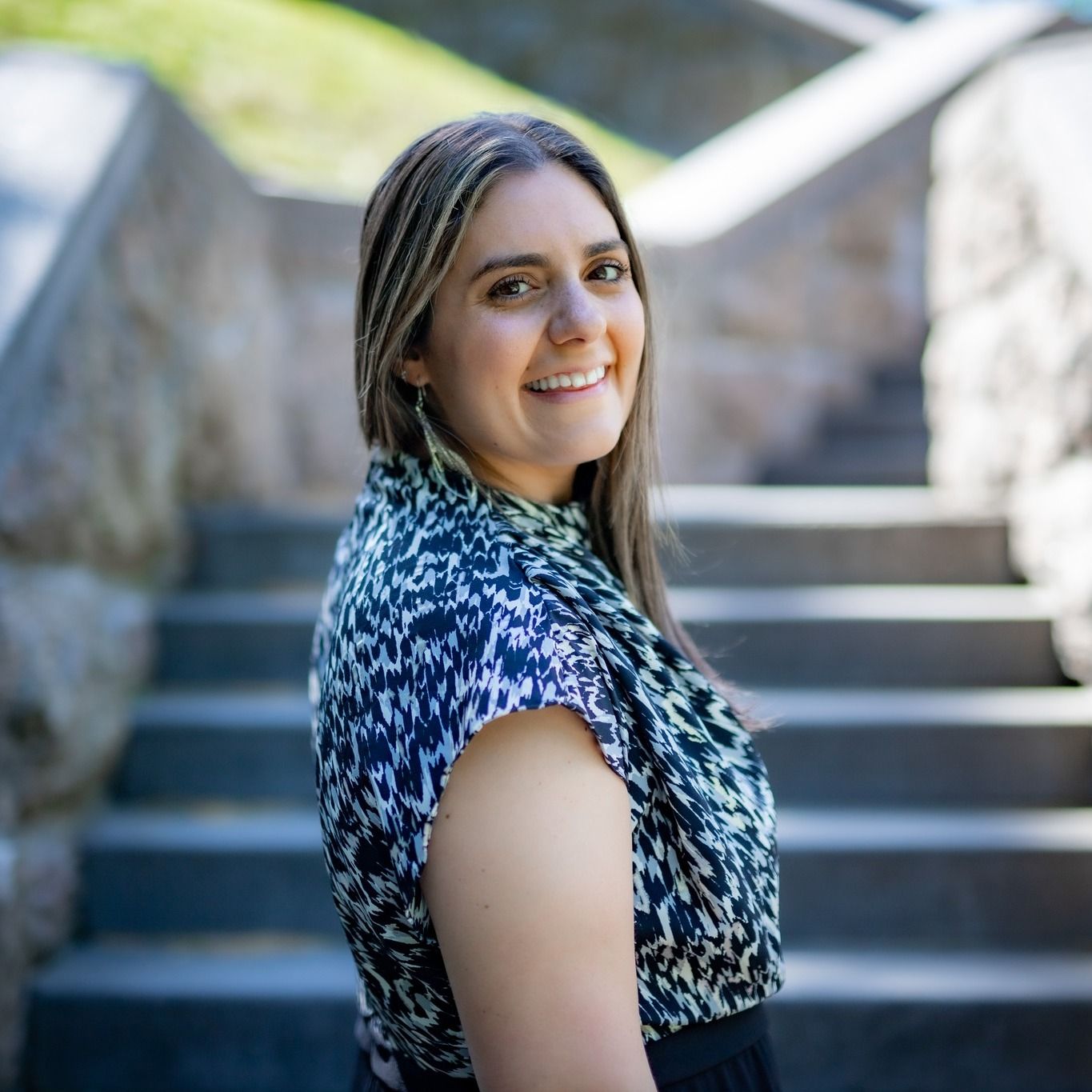 Portrait of woman in patterned dress smiling on outdoor staircase.
