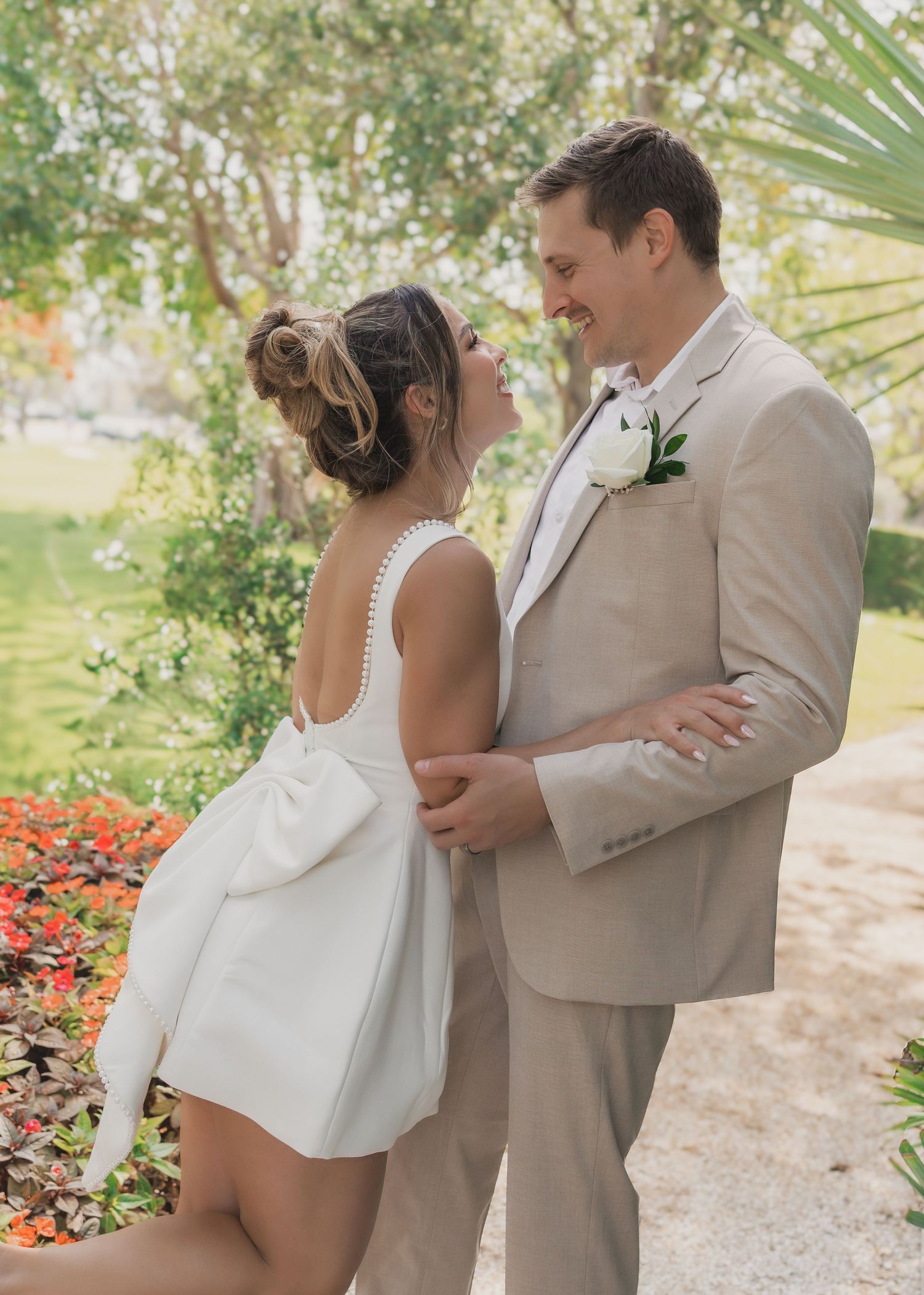 A joyful couple shares an intimate moment in a garden setting with palm trees and red flowers in the background.