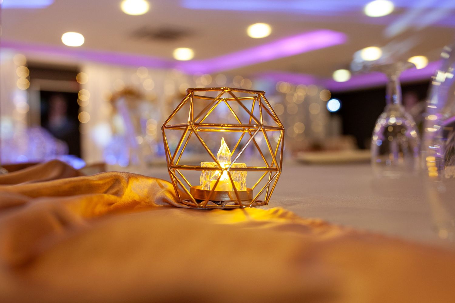 Geometric gold wire candle holder glowing warmly on table at evening event.
