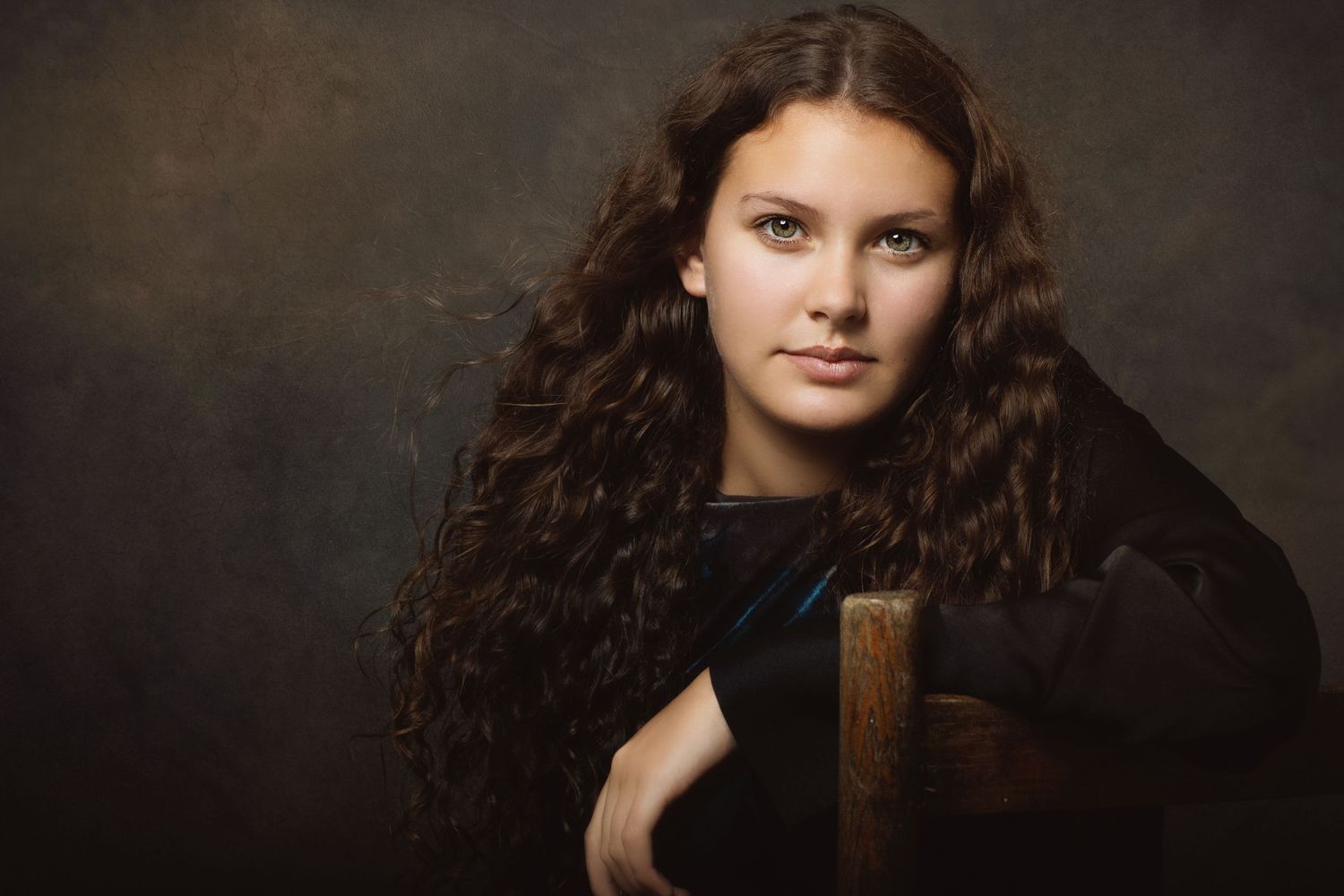 Professional studio portrait series with a dramatic artistic lighting style highlighting rich brown curls against a dark background.