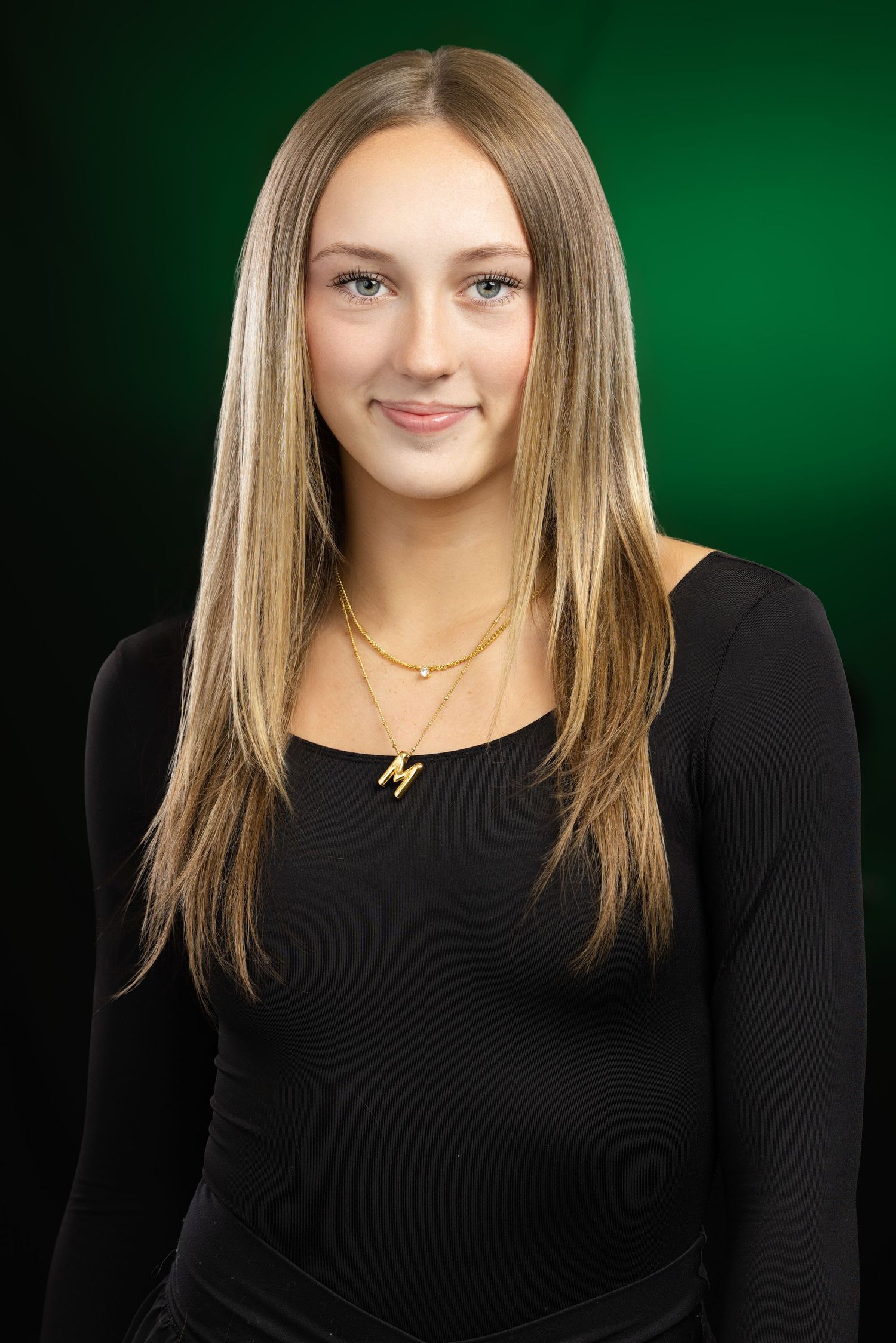 Studio portrait wearing black top and gold necklace against green background.