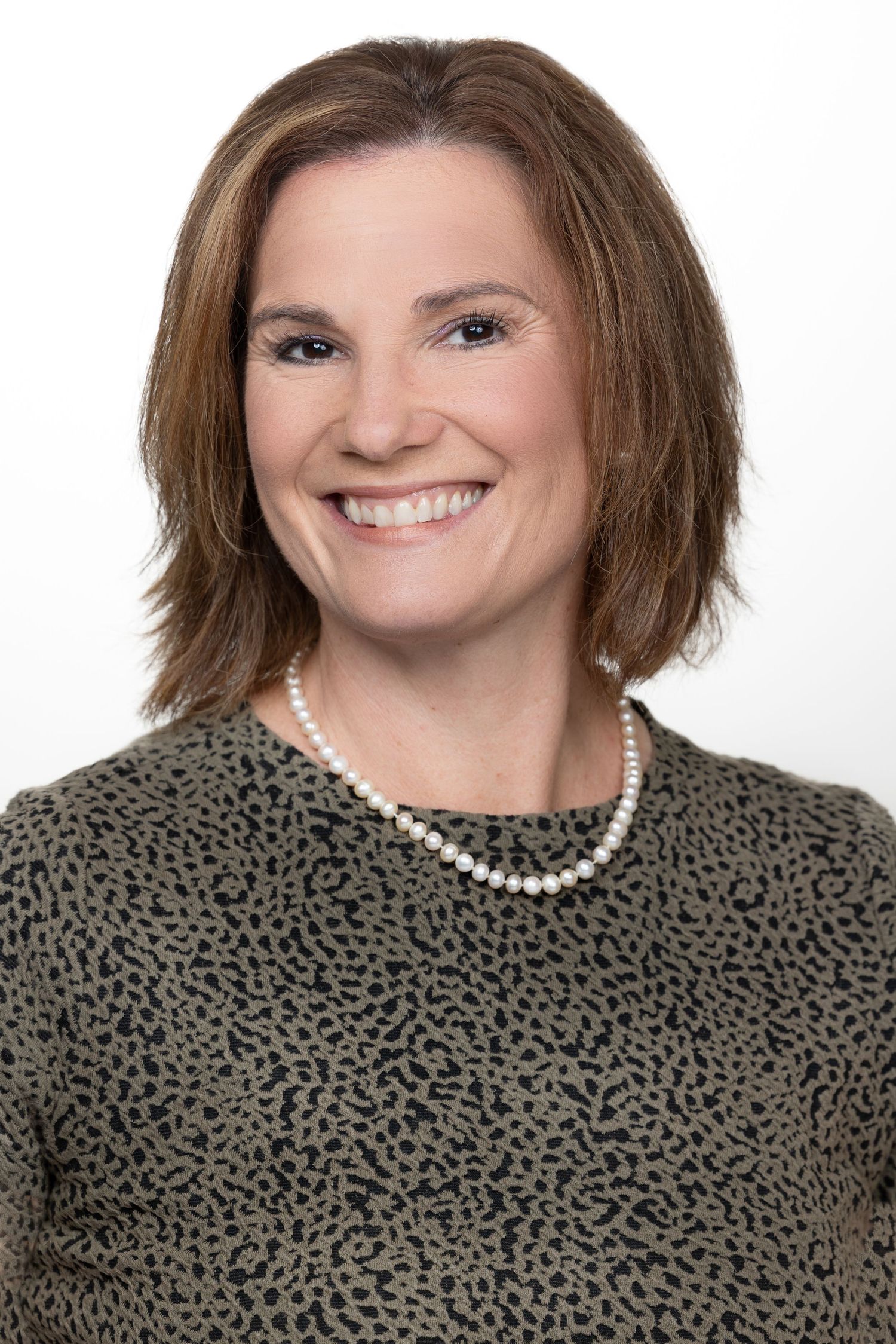 Professional headshot of a person wearing a textured dark sweater and pearl necklace against white background.