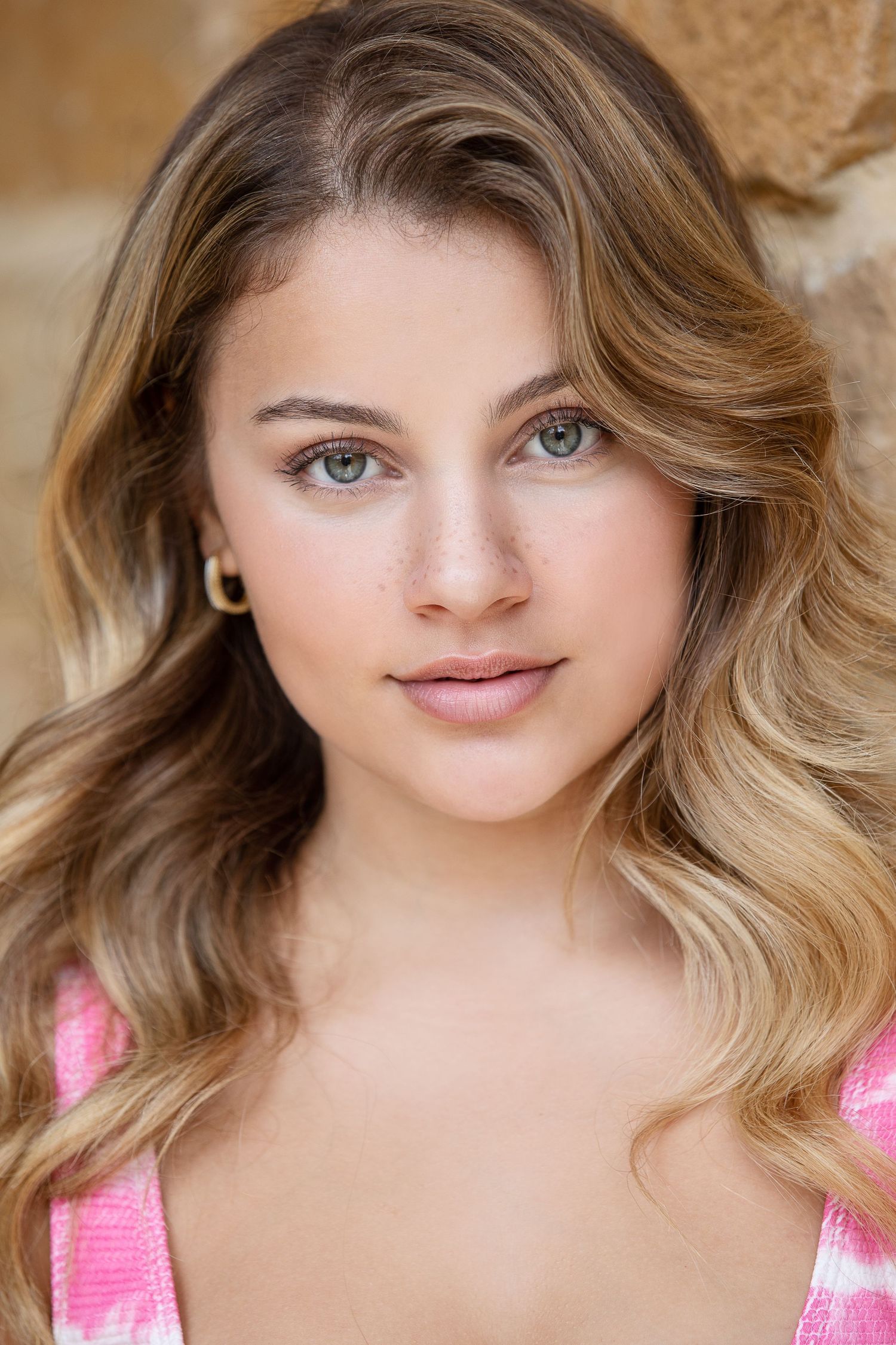 Portrait of a young woman with wavy blonde hair wearing a pink and white top.