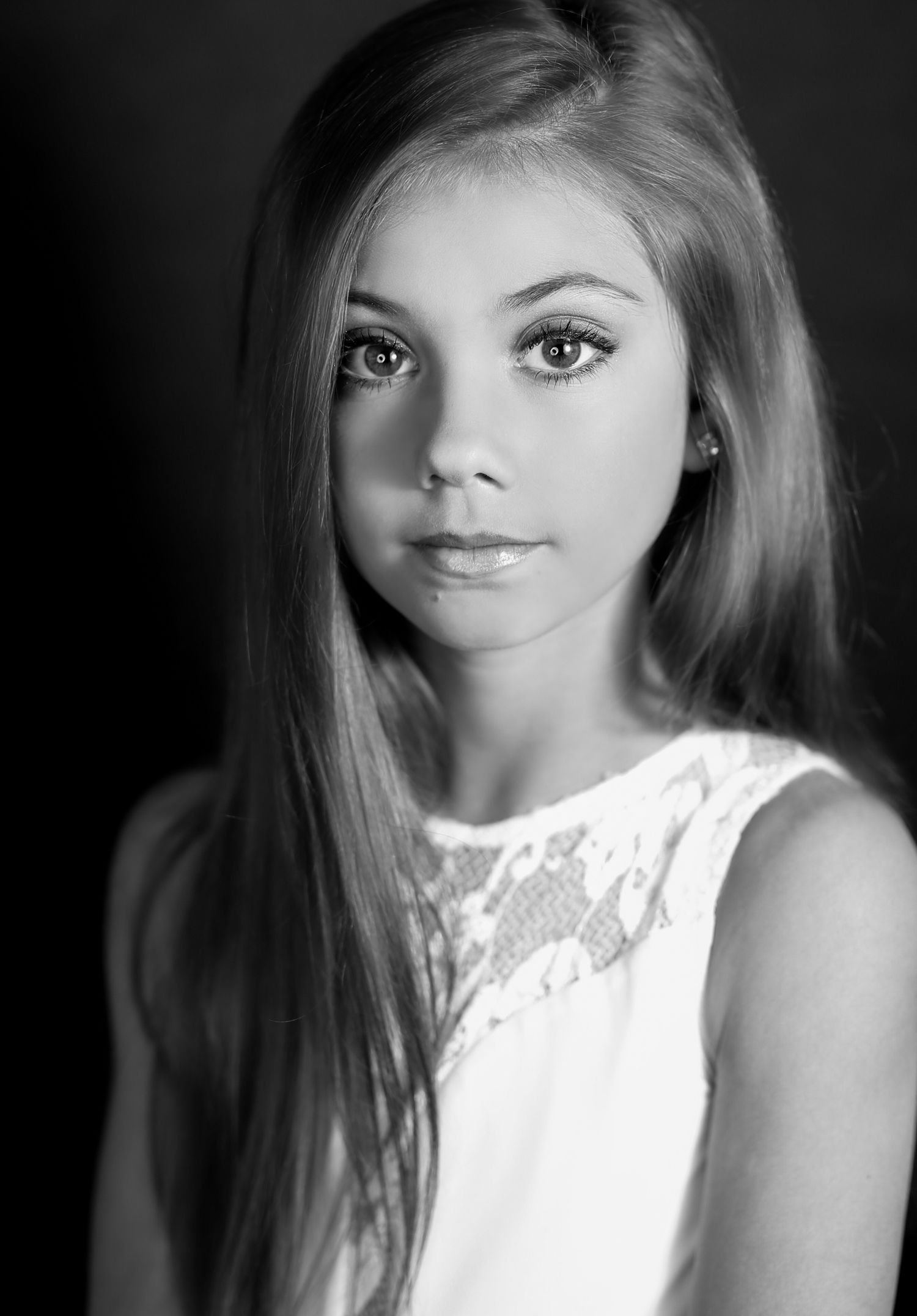 Black and white portrait photograph showing a young woman with long blonde hair wearing a white lace sleeveless top.