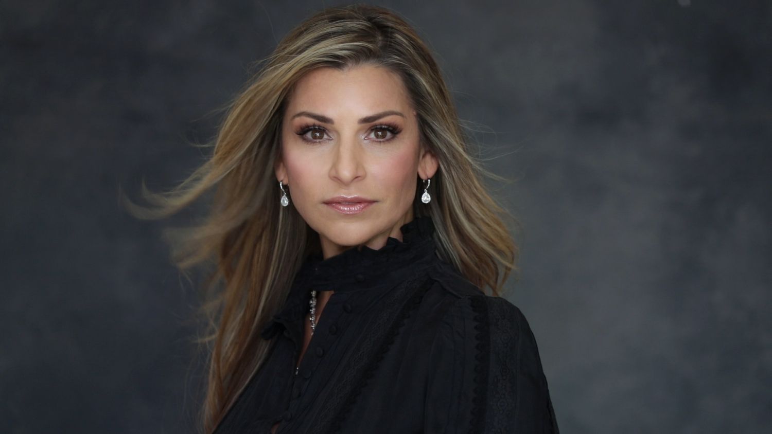 Professional studio portrait of woman in black top with dramatic lighting against dark background.