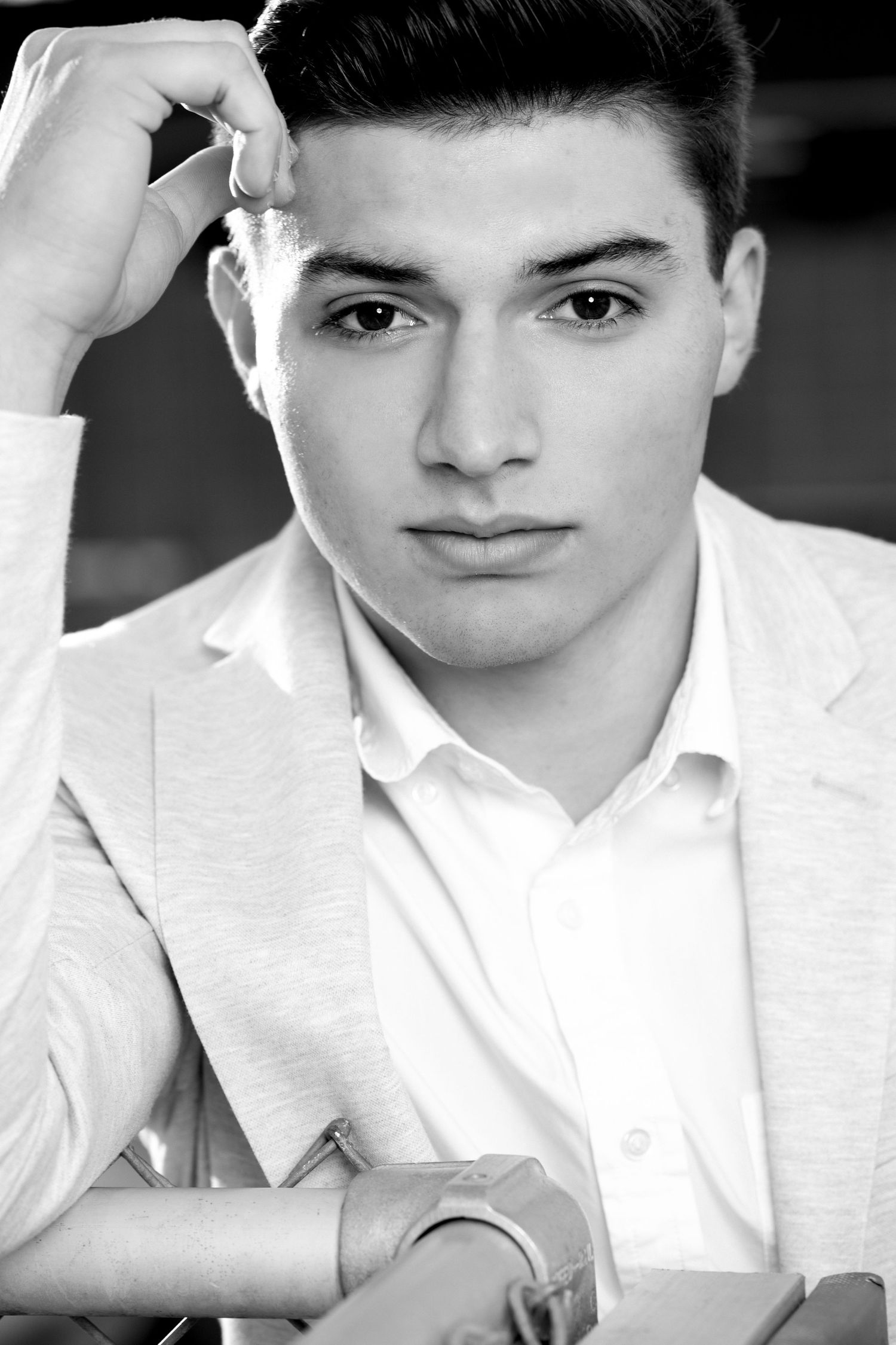 Black and white portrait photograph of a young person in a white blazer and shirt against a dark background.