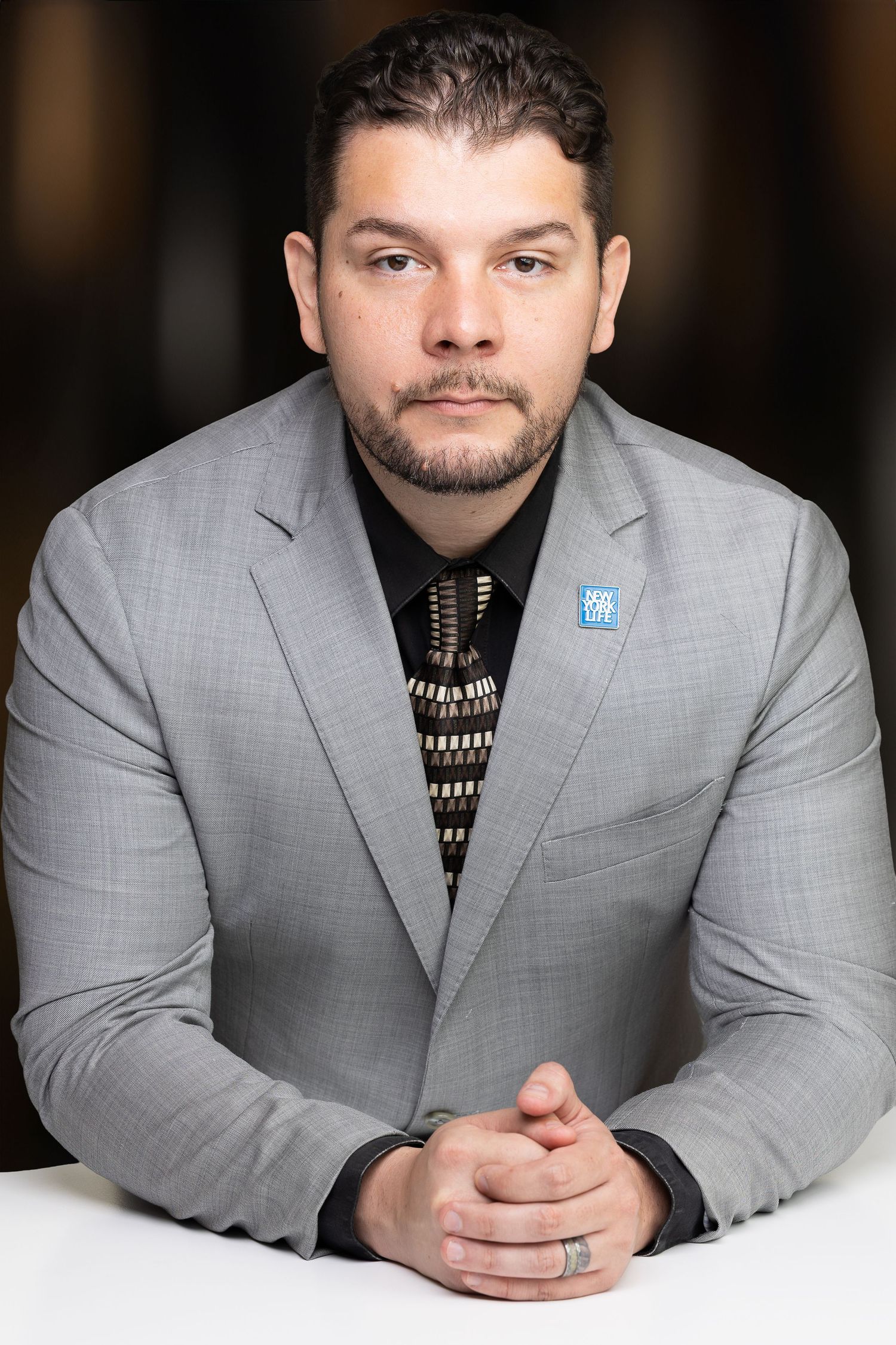Professional headshot series of someone wearing a gray blazer and patterned sweater while posing against dark background.