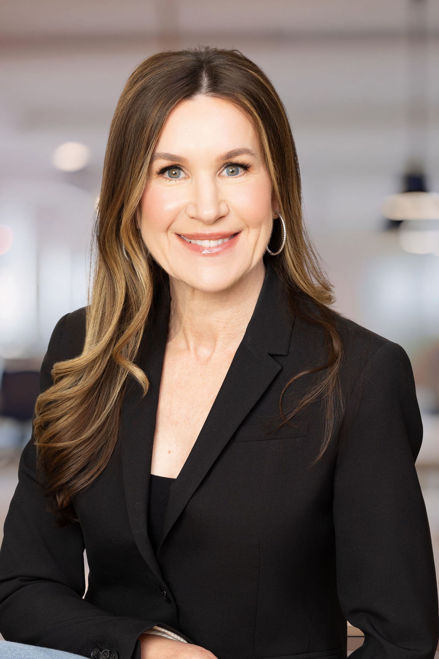 Professional headshot photo showing subject wearing a black blazer in corporate office setting.