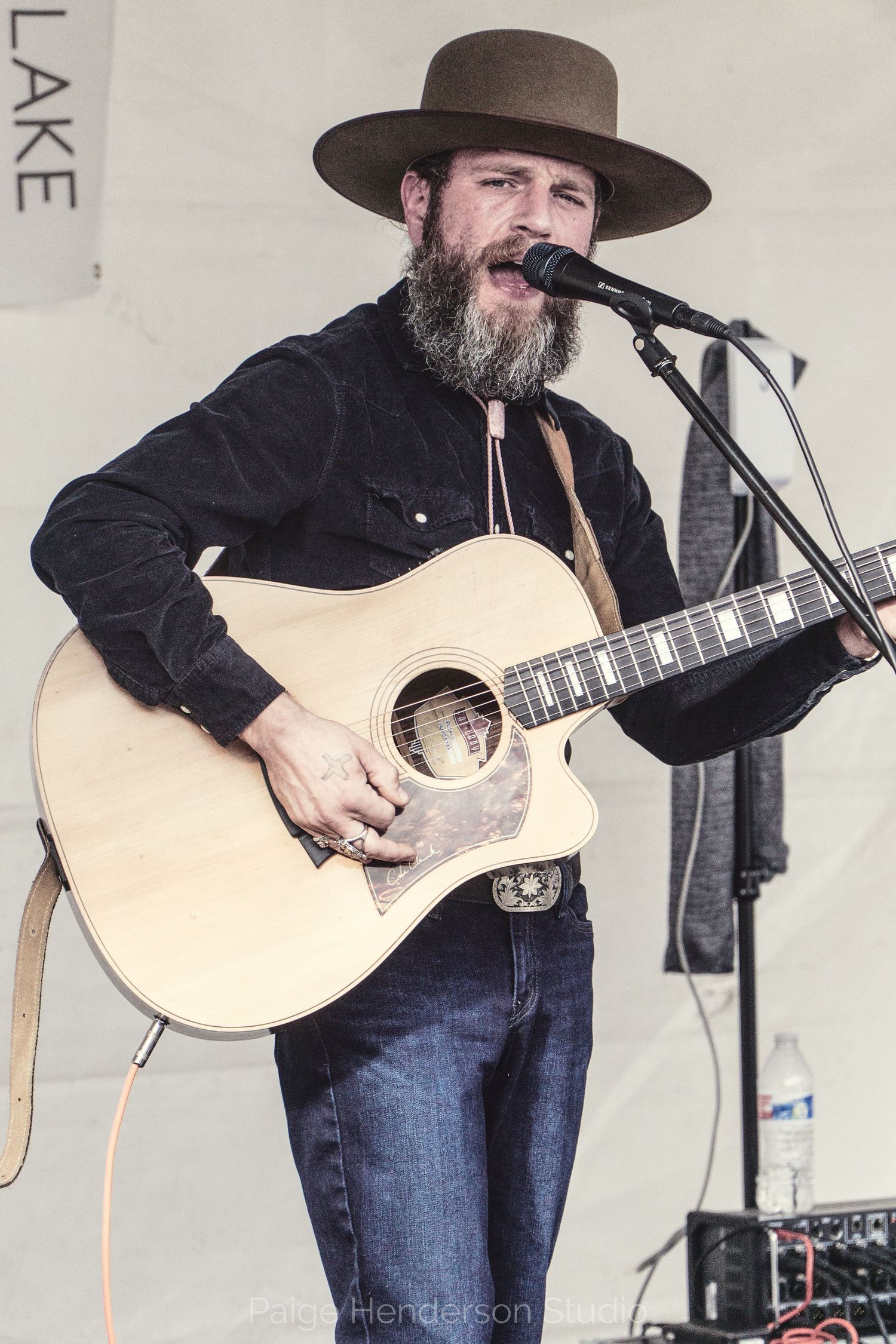 Musician in black shirt and cowboy hat plays acoustic guitar on stage during a live performance.
