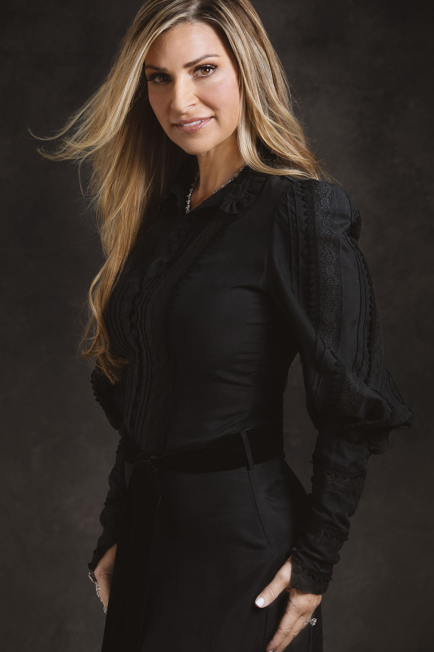 Professional studio portrait of woman in elegant black dress with dramatic lighting and textured background.
