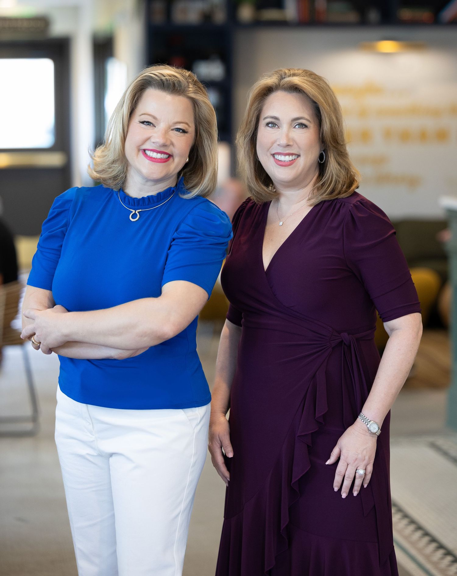Two professionals in business attire stand side by side smiling warmly in an office setting. Photo by Bellus Photography, Paige Henderson