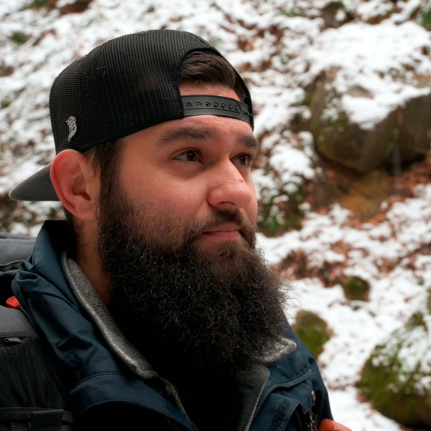 Winter outdoor portrait featuring warm clothing and beard against snowy mountain backdrop.