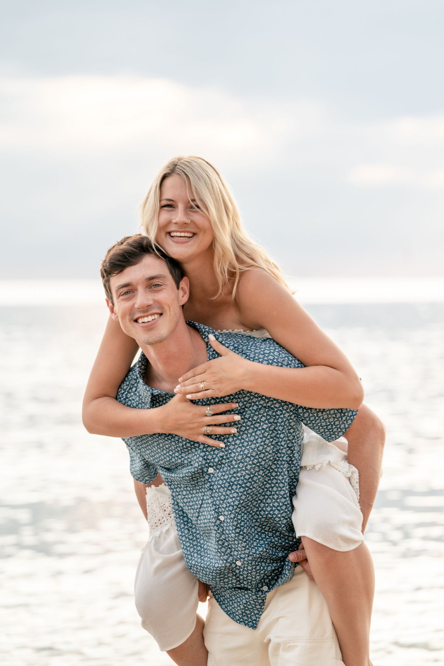 A couple enjoys playful piggyback rides along the beach in a series of white and blue-tinted photos at sunset.