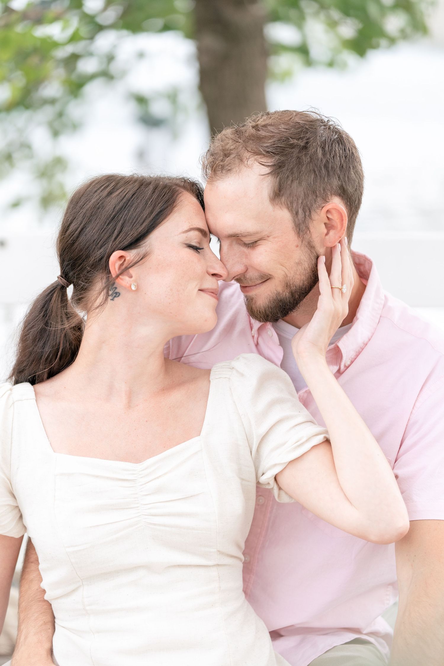 A romantic couple shares an intimate moment outdoors, wearing pink and white shirts with soft lighting in the background.