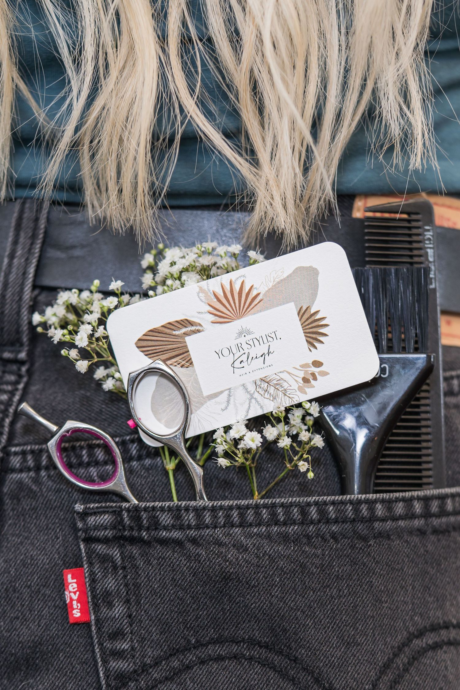 A white product tag with graphics is attached to a dark denim pocket with floral decorations.