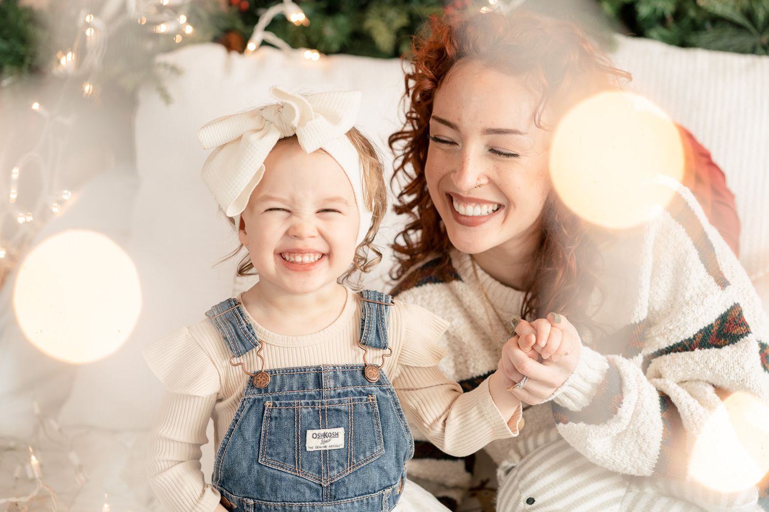 A toddler in overalls sits against a white backdrop with soft LED string lights creating a warm glow.