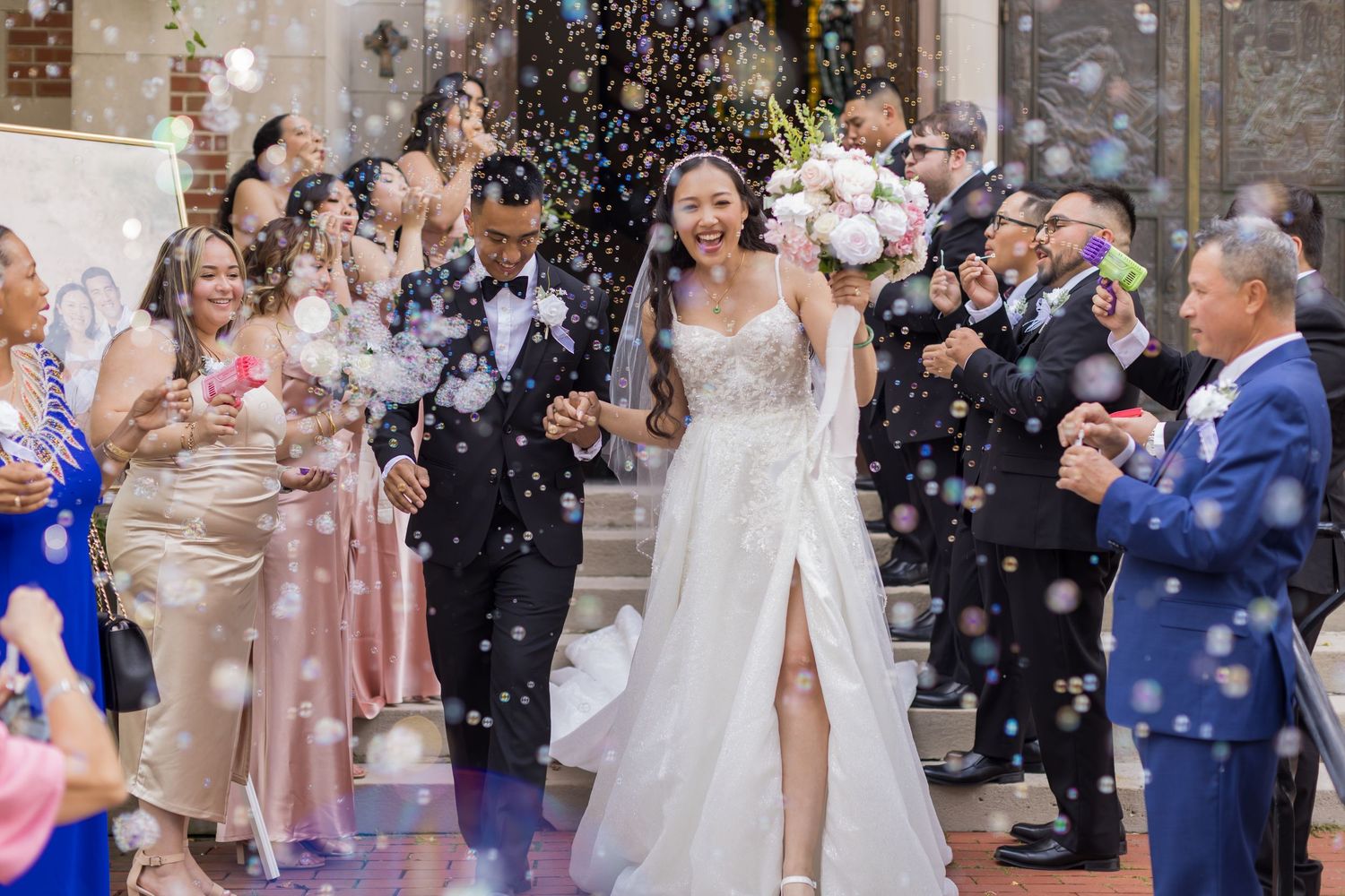 A couple exits their wedding ceremony while guests shower them with confetti in front of a stone church.