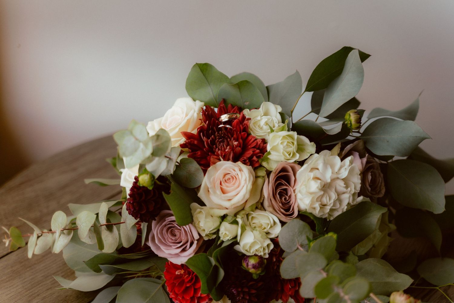 Elegant wedding bouquet with white and burgundy roses mixed with eucalyptus leaves on wooden surface.