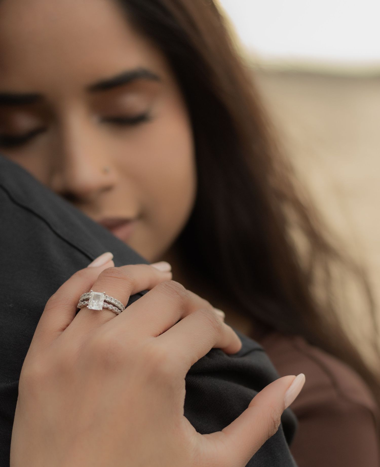 Close-up detail of an elegant engagement ring being worn while embracing in a soft natural light.