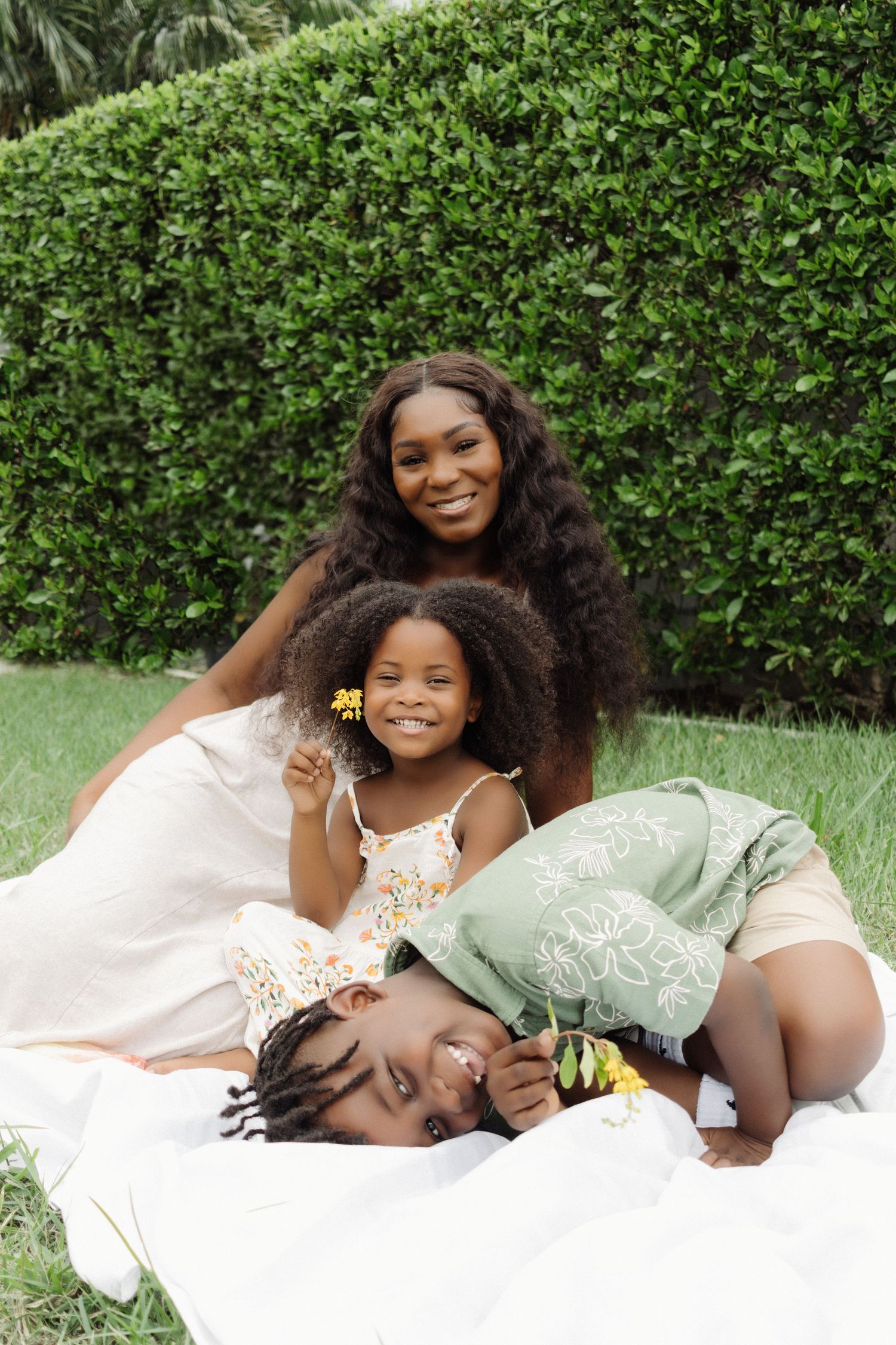 A playful outdoor family portrait captured against a lush green hedge backdrop.