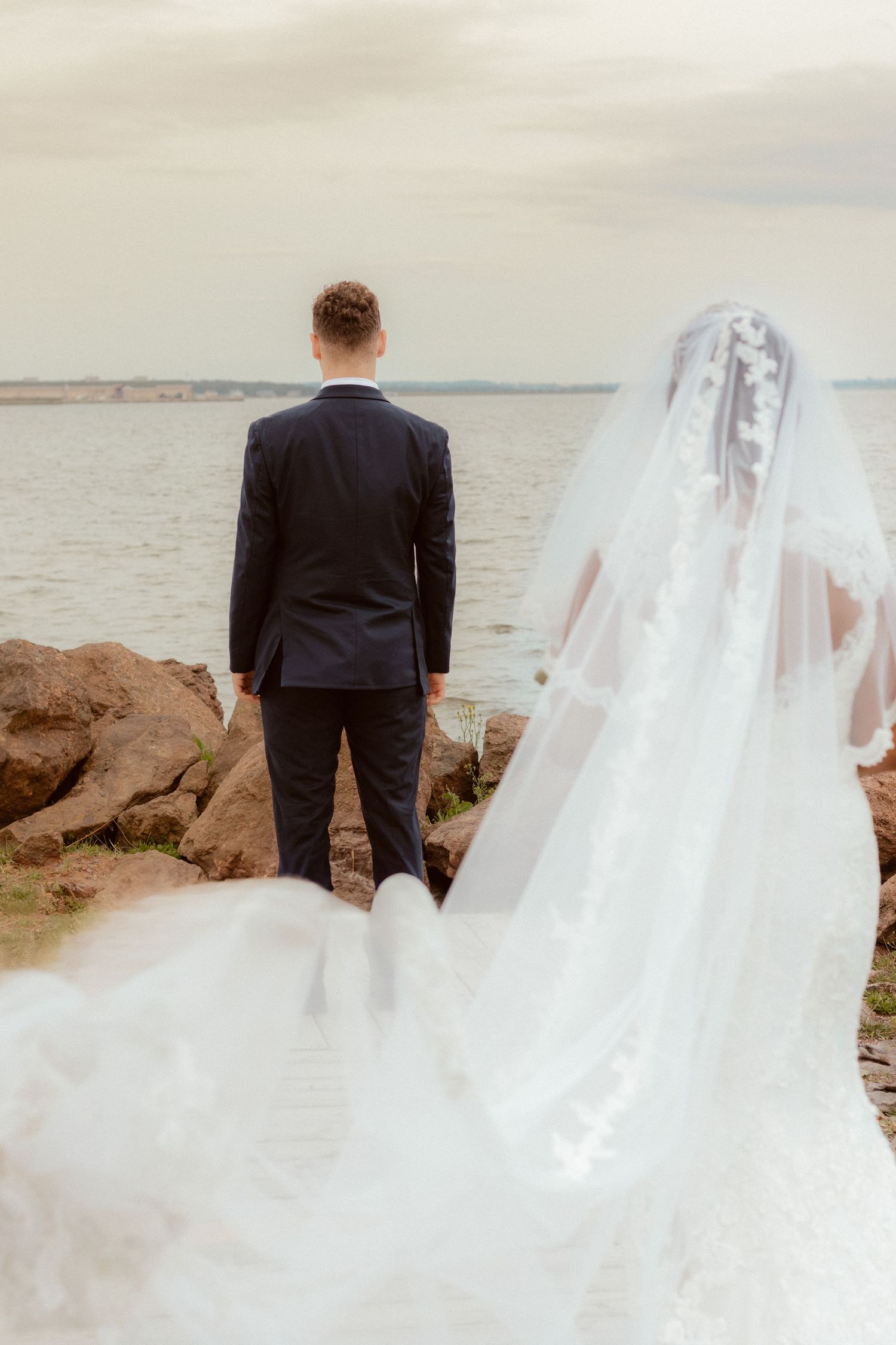 Bride and groom standing on rocky coastline overlooking the ocean during their wedding.