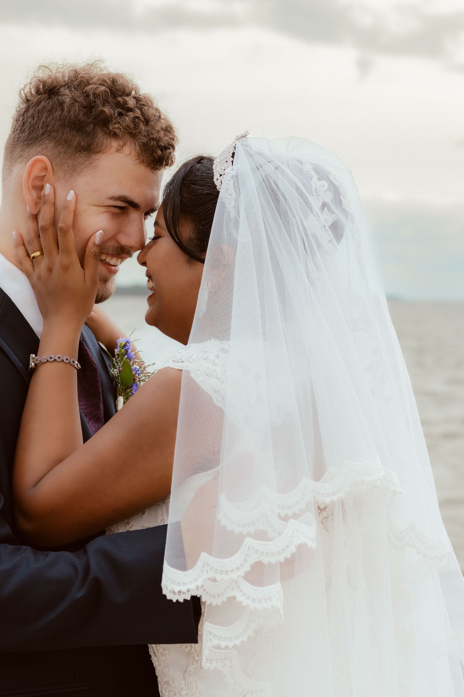 Tender moment between newlyweds on their wedding day by the ocean.