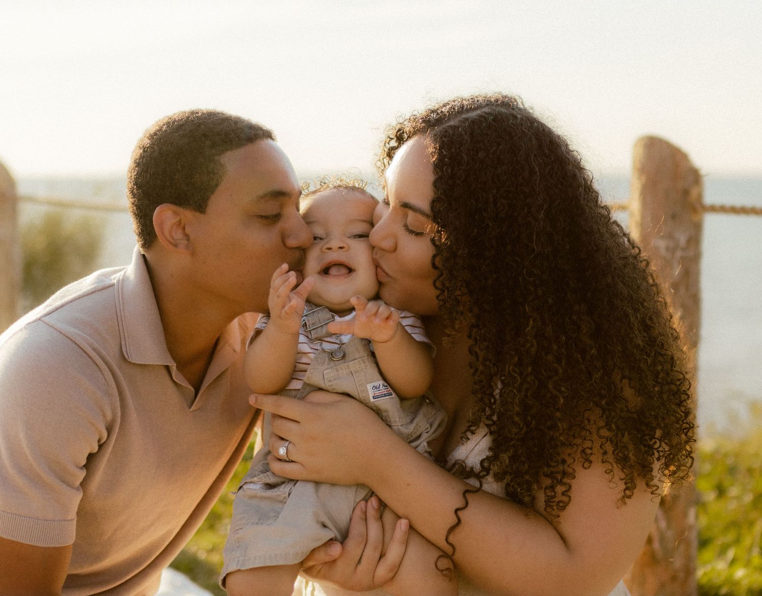 Family shares joyful kisses with their baby during golden hour outdoor photo session.