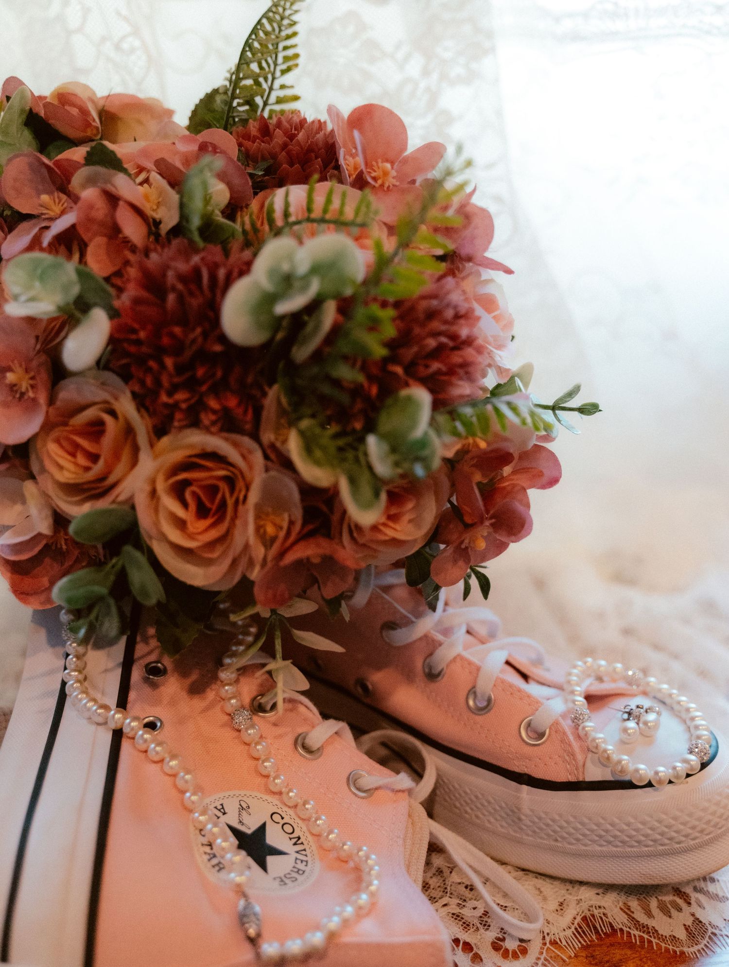 A pink Converse sneaker filled with coral roses, eucalyptus, and ferns arranged as a creative floral centerpiece.