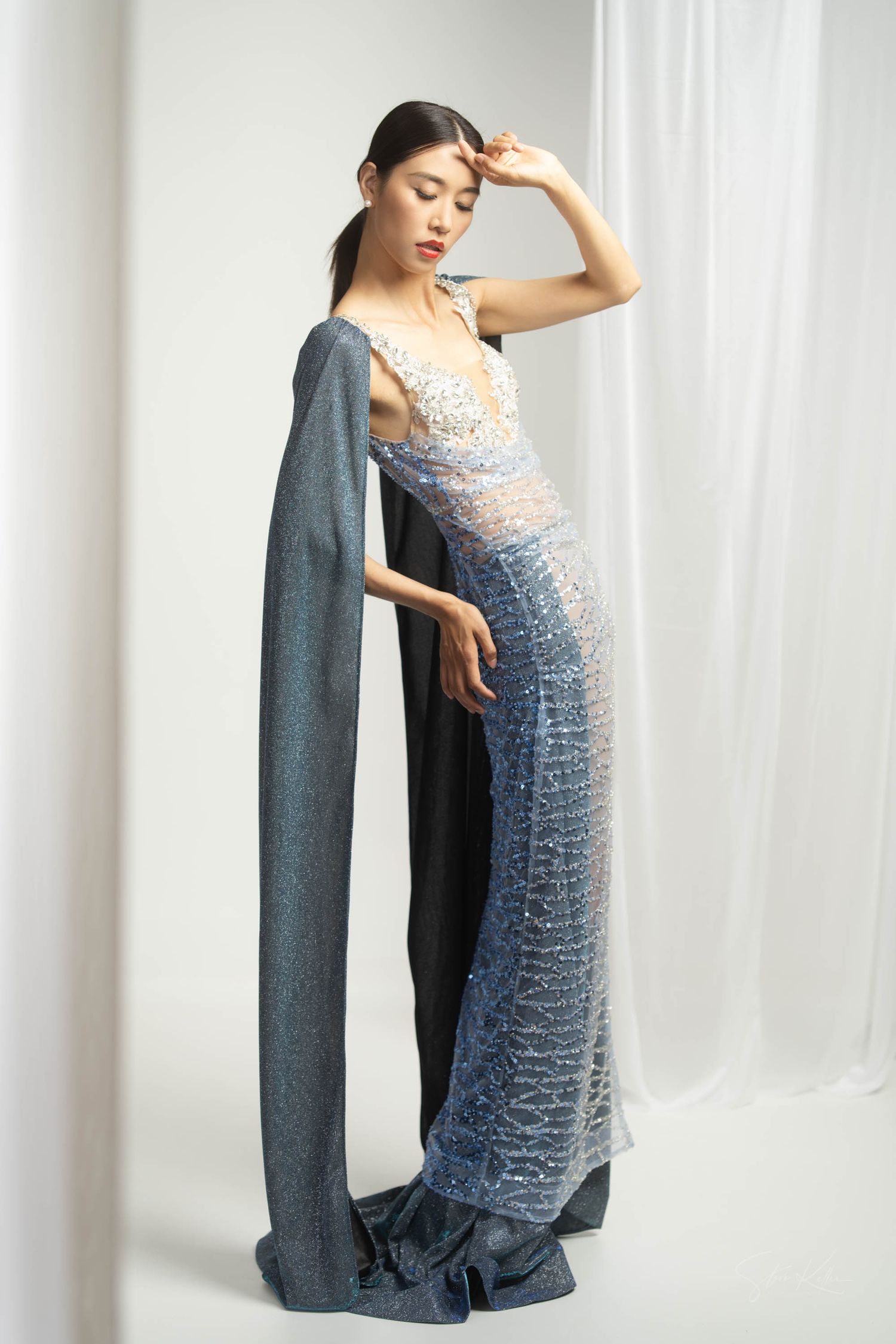 A figure poses in an elegant blue ombre evening gown with sequins against a white backdrop.