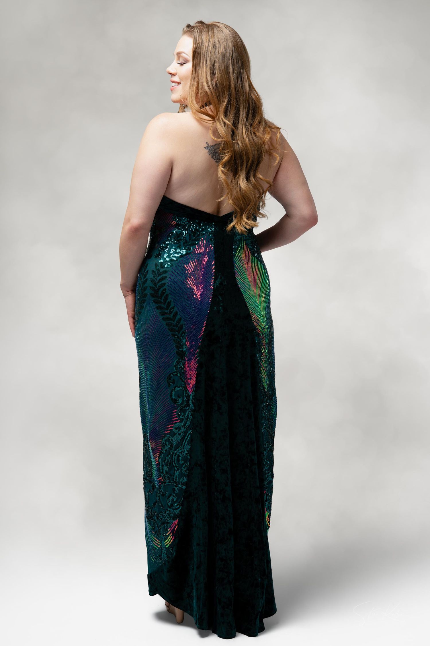 Back view of a strapless evening gown in dark teal with iridescent pattern details.
