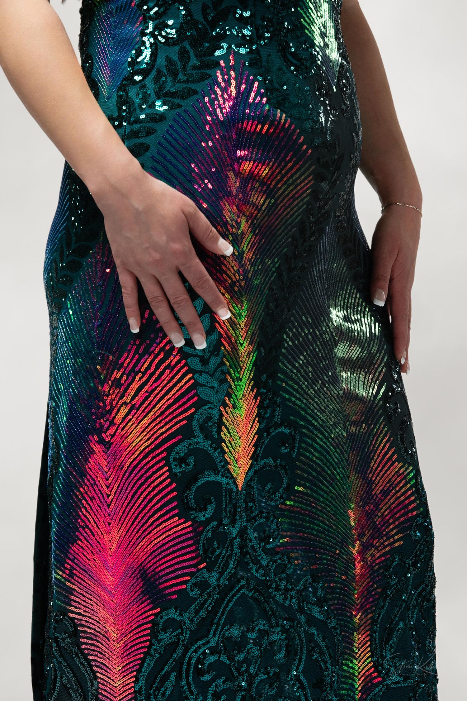Close-up of a sequined evening dress with vibrant peacock feather pattern in iridescent teal, pink and rainbow colors.