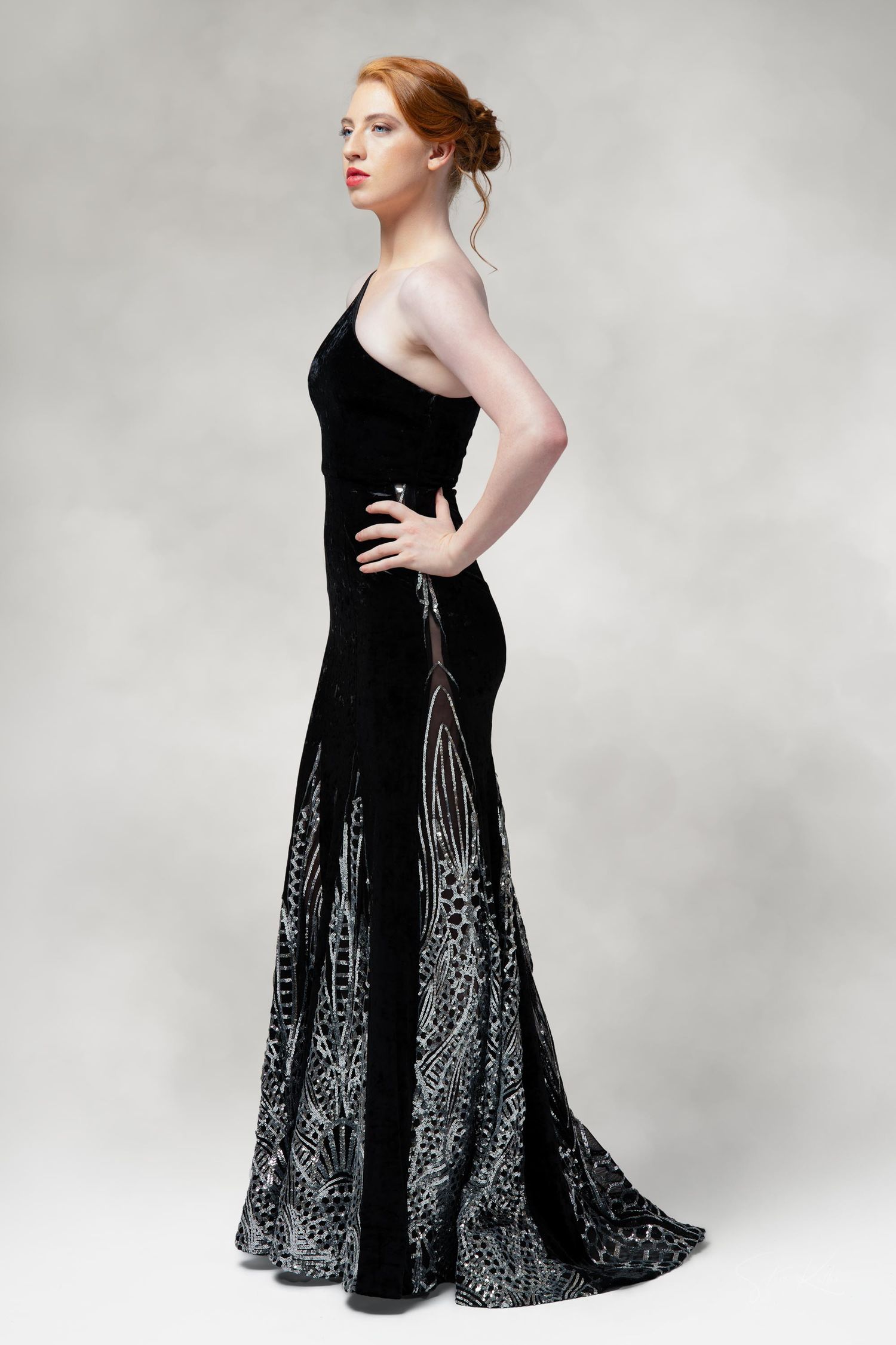 Person wearing an elegant black evening gown with silver embellishments posed against a gray backdrop.