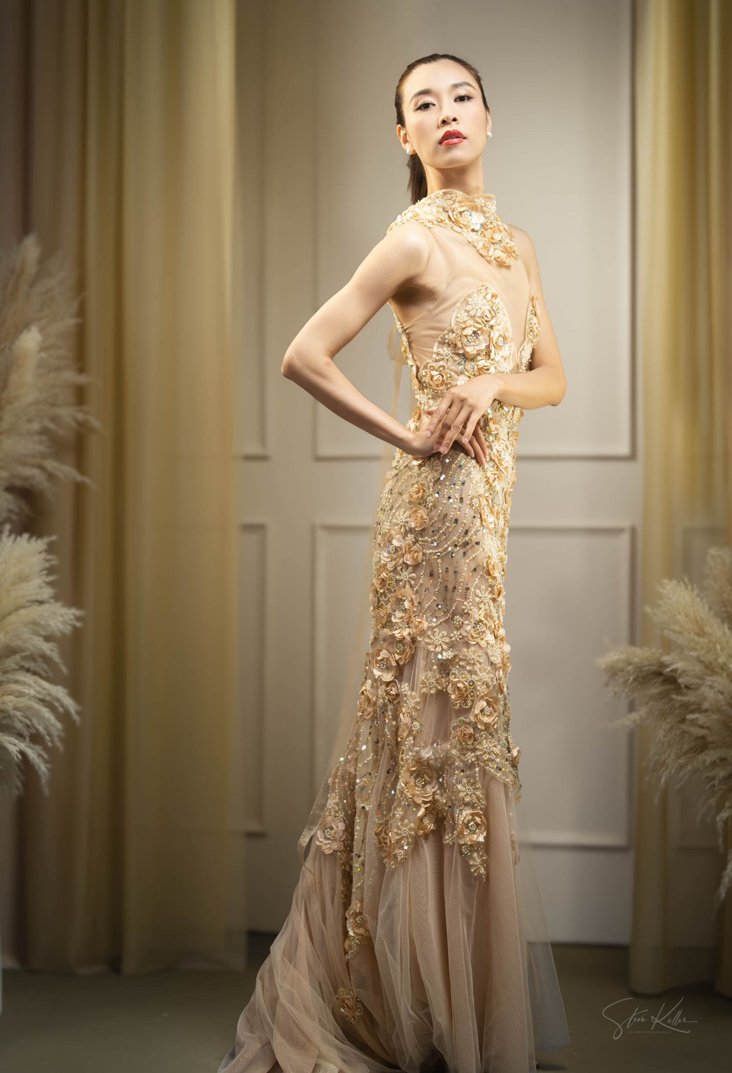 Elegant gold lace evening gown with intricate floral embellishments and sheer tulle skirt in a luxury room setting.