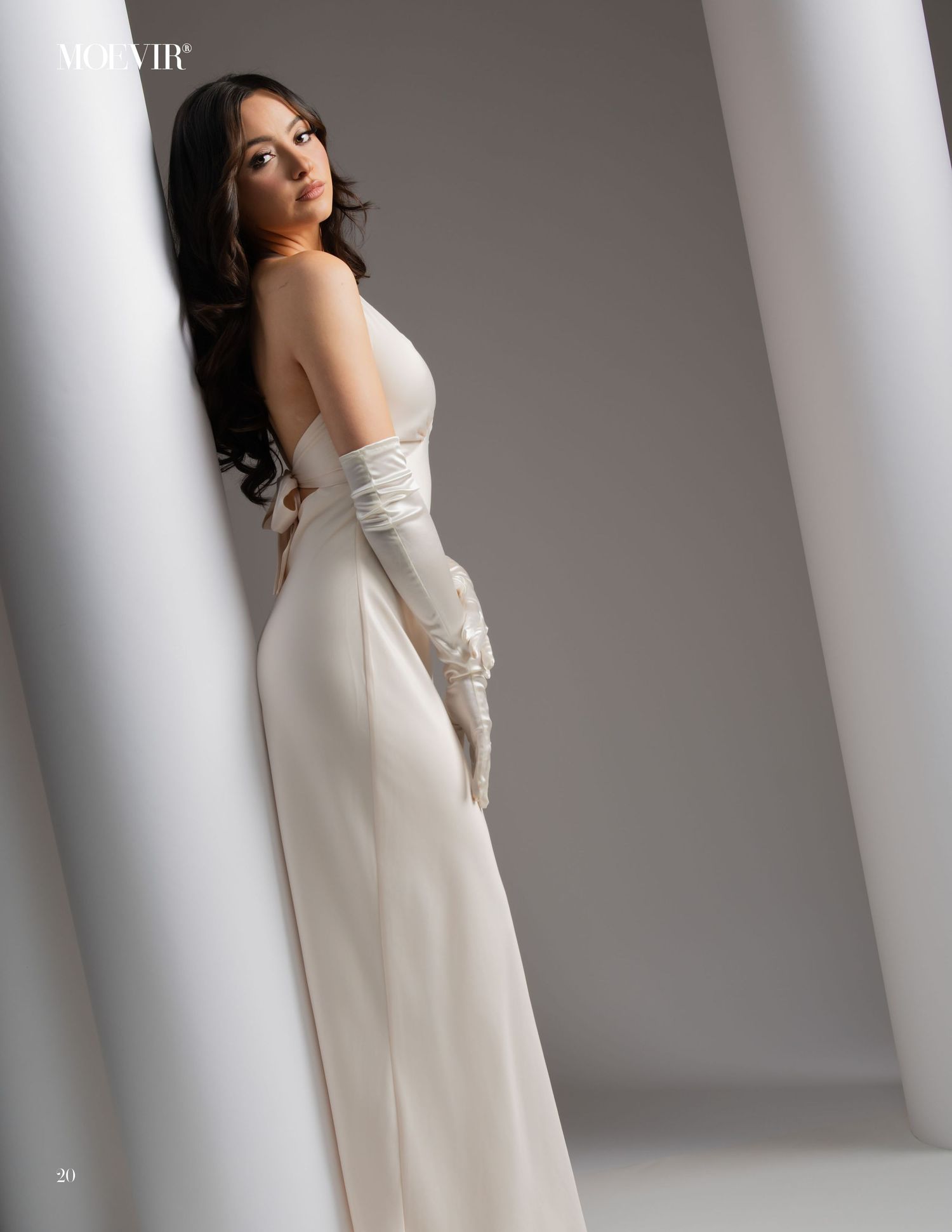 An elegant white column gown with long gloves photographed against a modern architectural backdrop with white pillars.