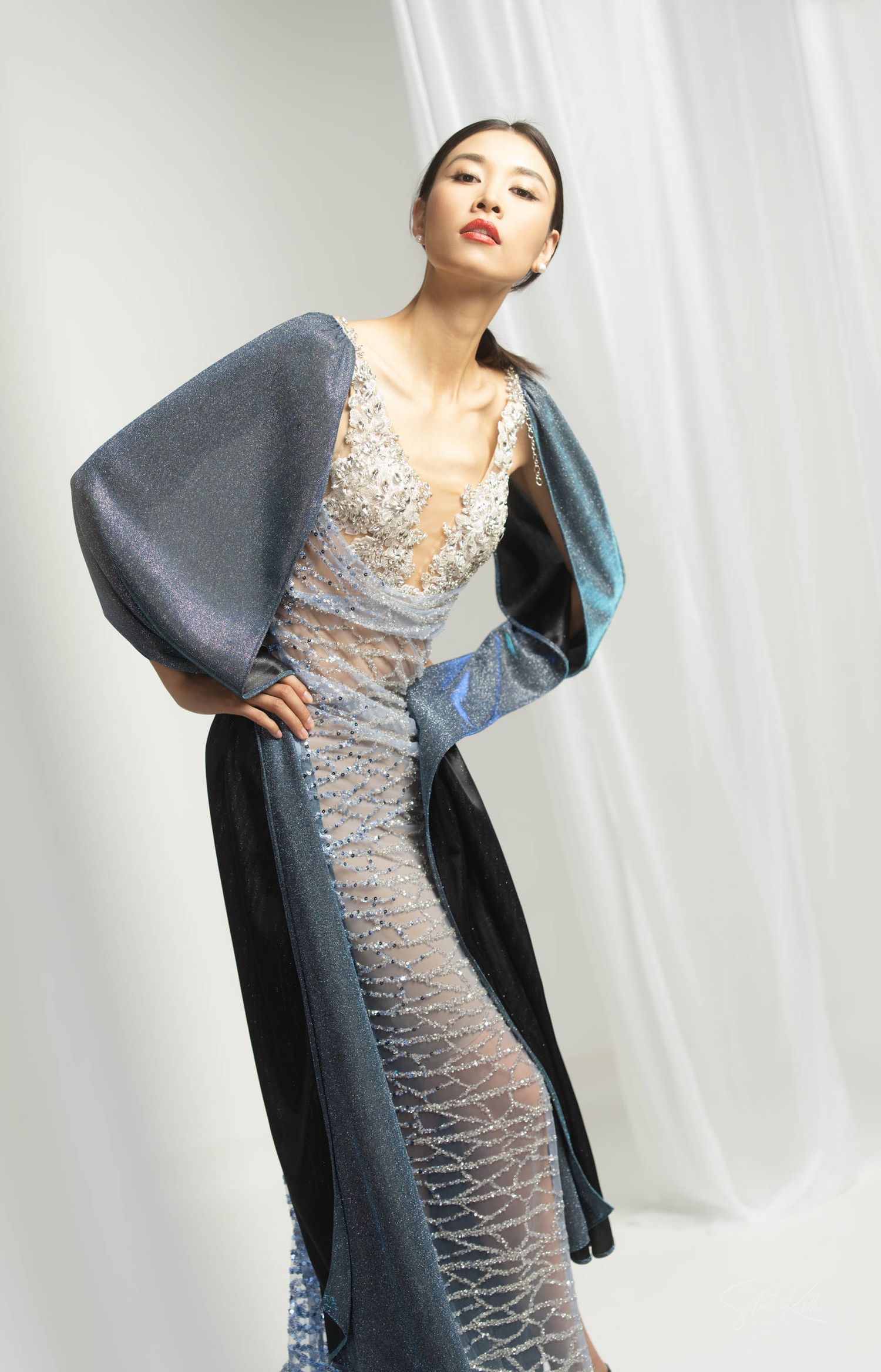 Fashion model poses in sheer lace gown with dramatic grey balloon sleeves against white backdrop.
