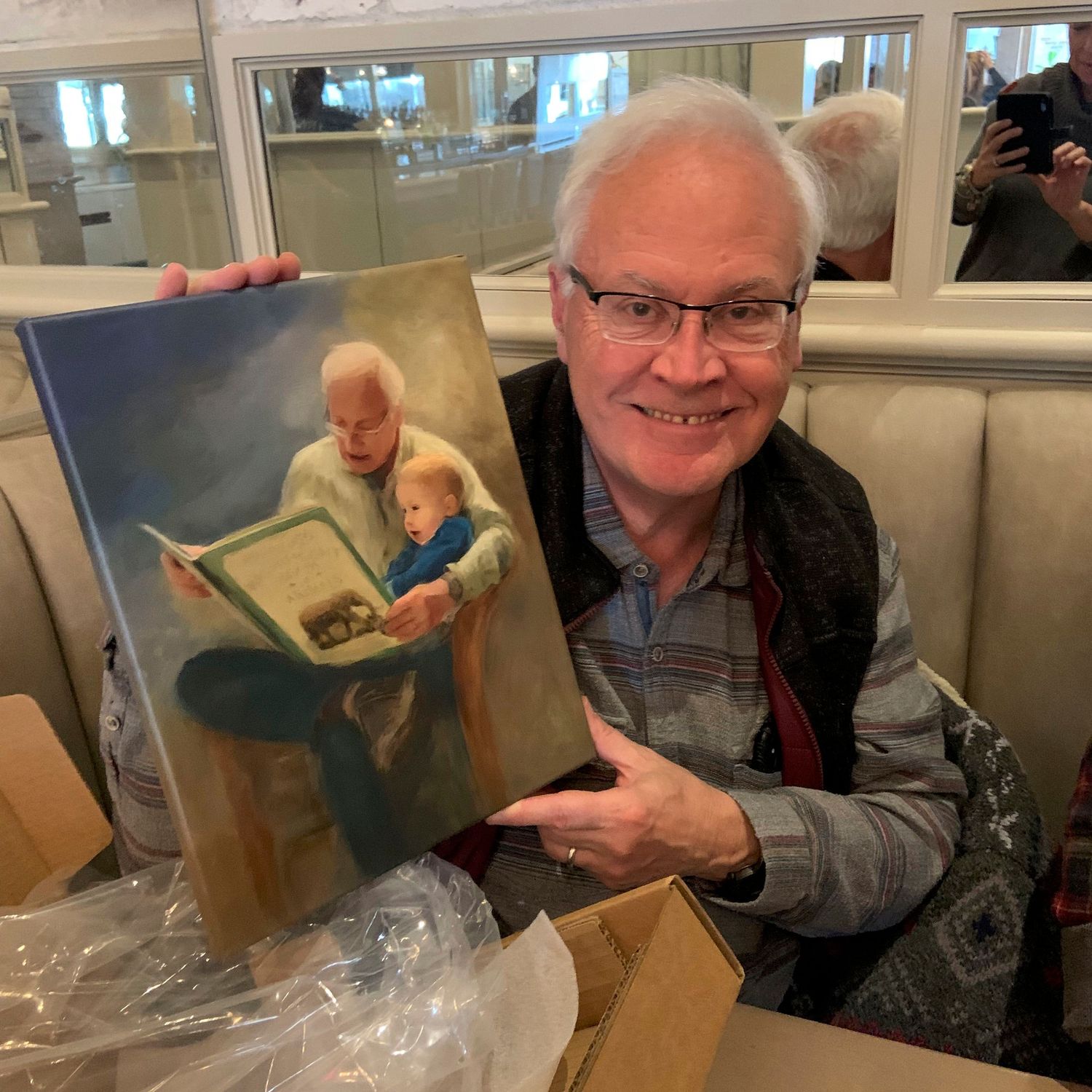 A very happy recipient of a painted portrait as a meaningful gift. The painting features him reading a book to his grandson.