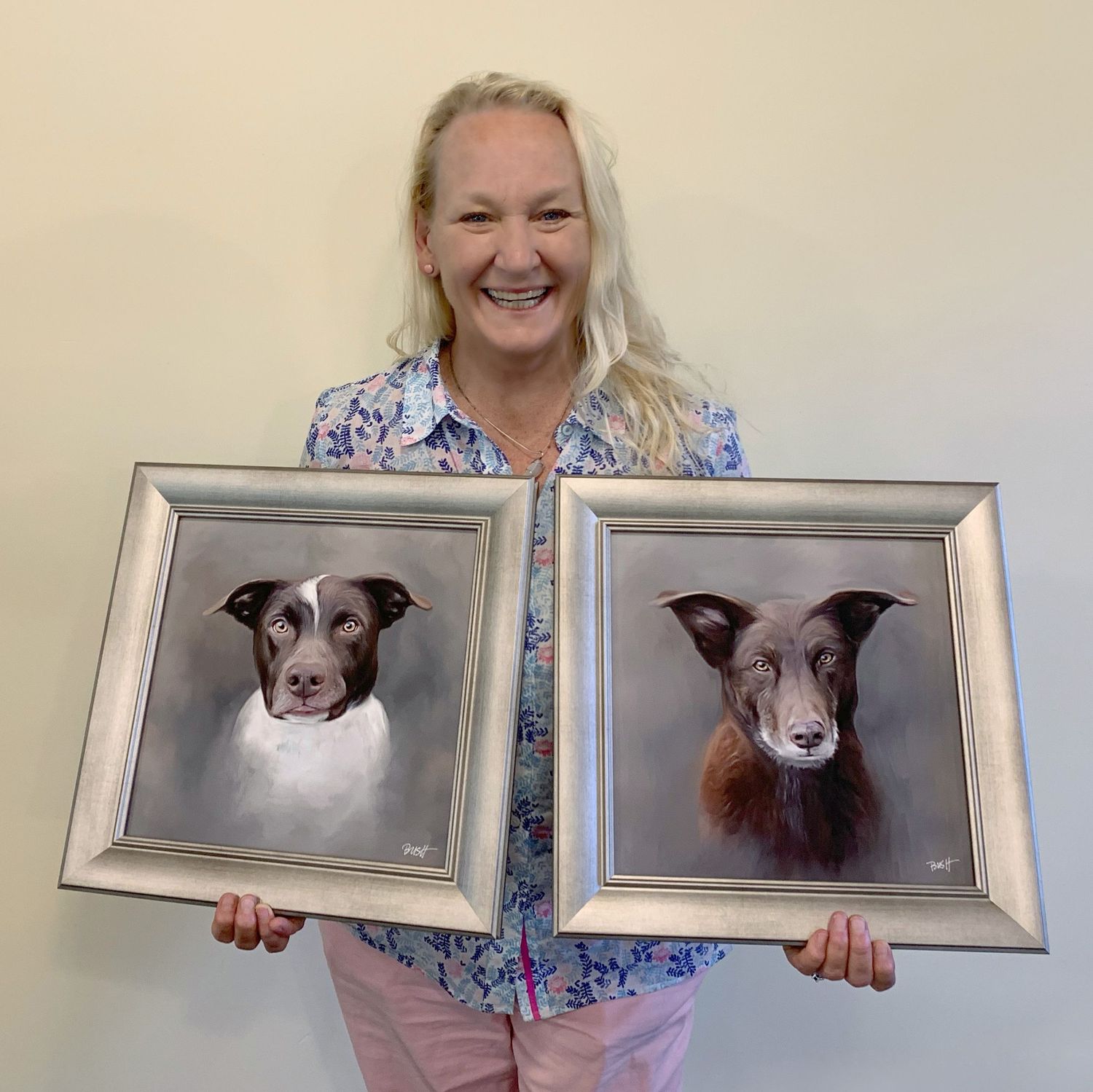 A very happy client proudly holding a pair of framed pet portrait paintings.