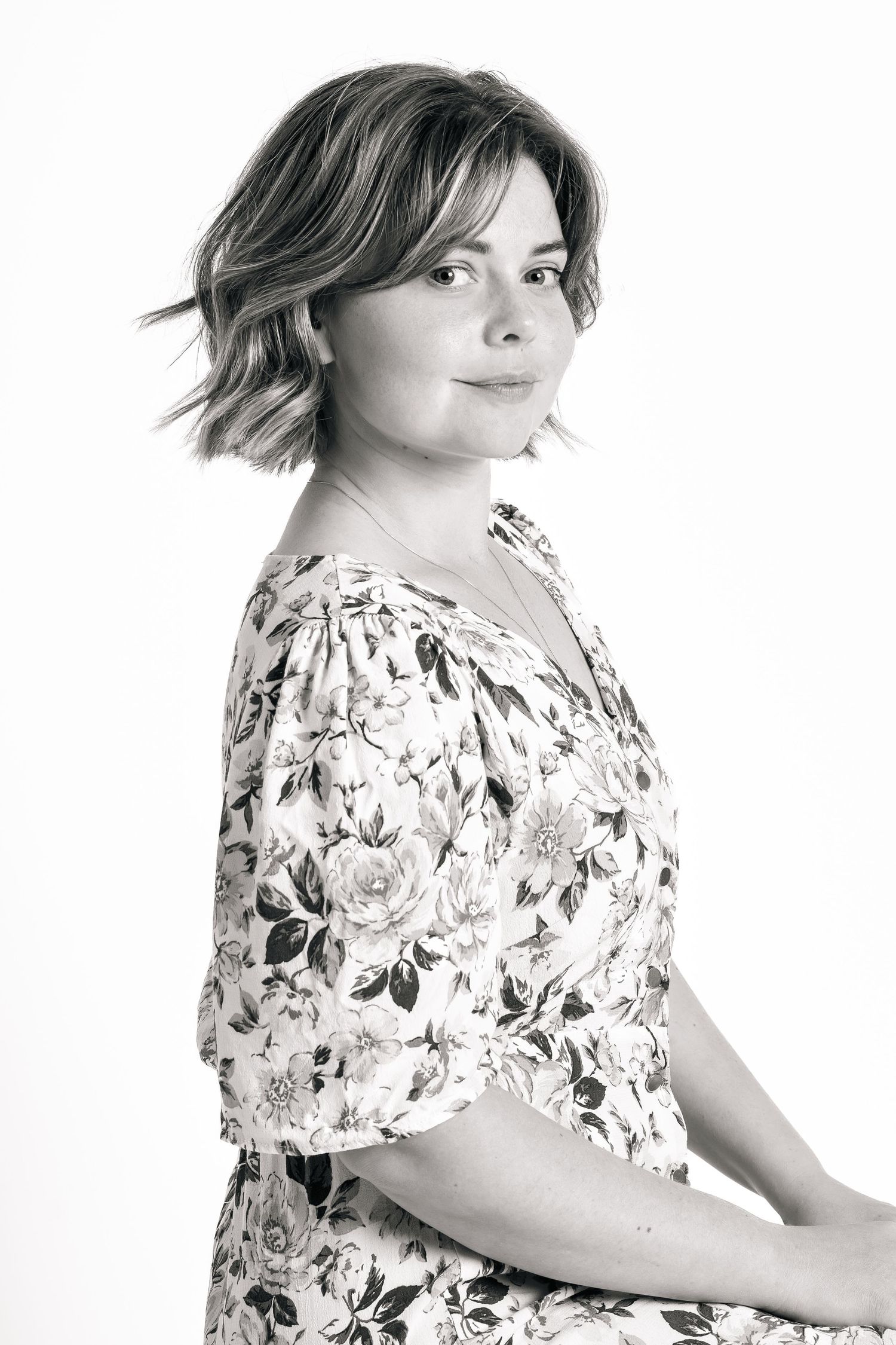 Black and white portrait photograph of someone wearing a floral print dress while posing against a white backdrop.