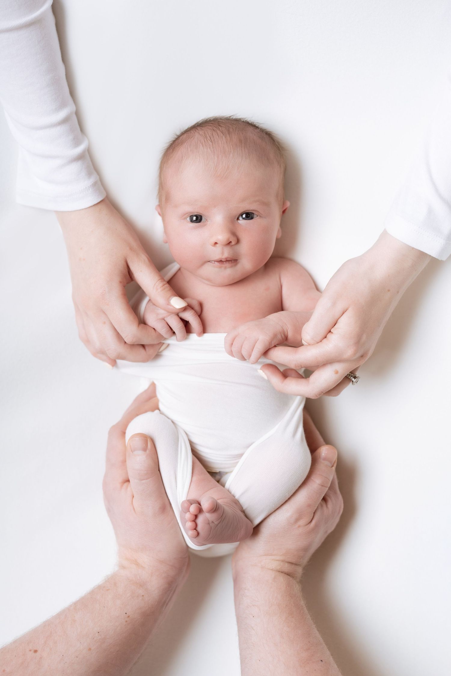 A baby wearing a white diaper is being held by adult hands against a light background.