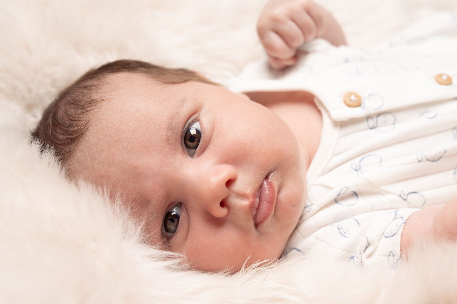 Young baby lying down on soft white bedding wearing light colored clothing.
