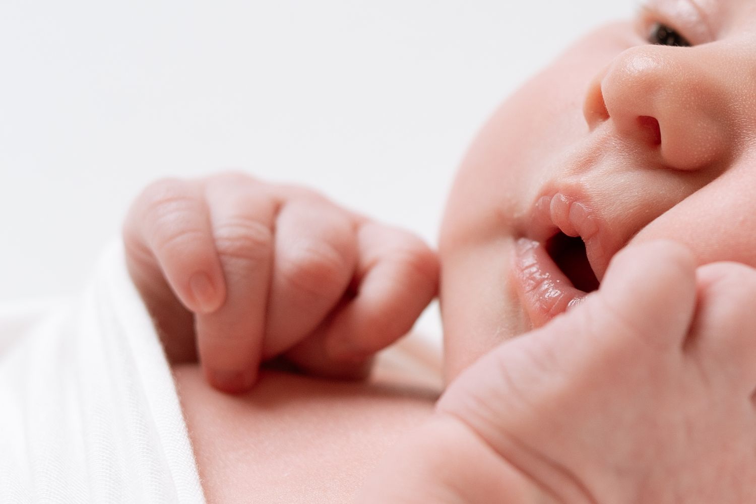 Small hand reaches toward infant's yawning mouth showing tender interaction between baby and parent.
