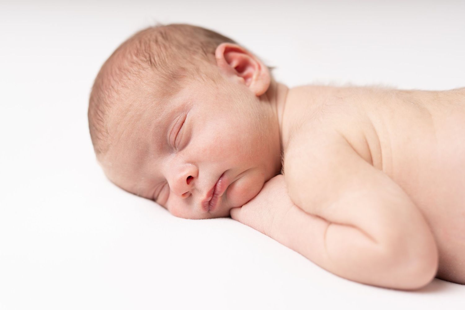 Peaceful sleeping newborn resting on white surface in natural light.