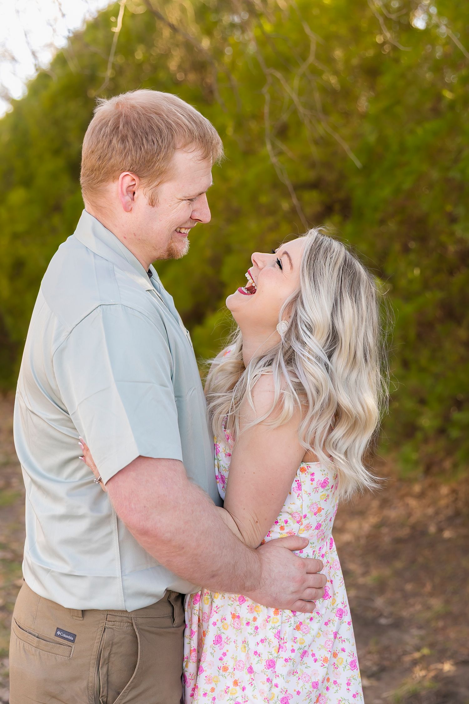 A couple embraces and laughs together outdoors wearing spring formal clothes during a family photoshoot in Pittsburg KS and Joplin MO.
