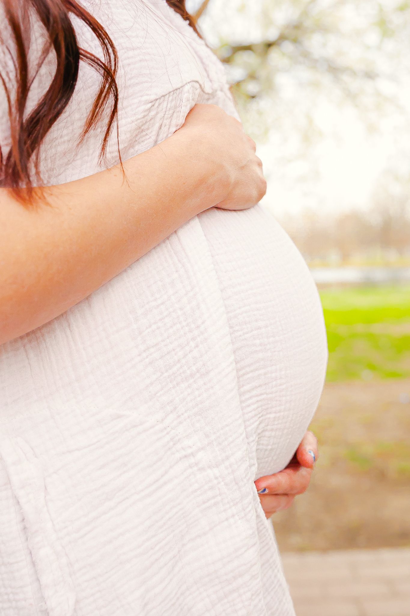 Profile of a pregnant belly with hands cradling the bump, wearing a white dress outdoors for maternity photos in Pittsburg KS and Joplin MO.
