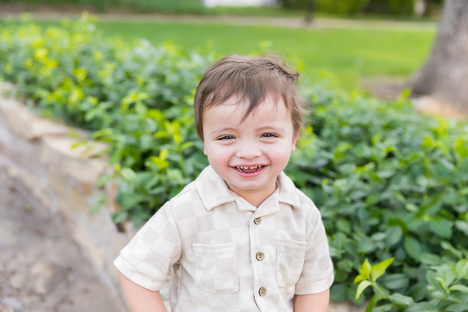 A smiling child in a collared shirt poses near green foliage for a 2nd birthday milestone photoshoot in Pittsburg KS and Joplin MO.