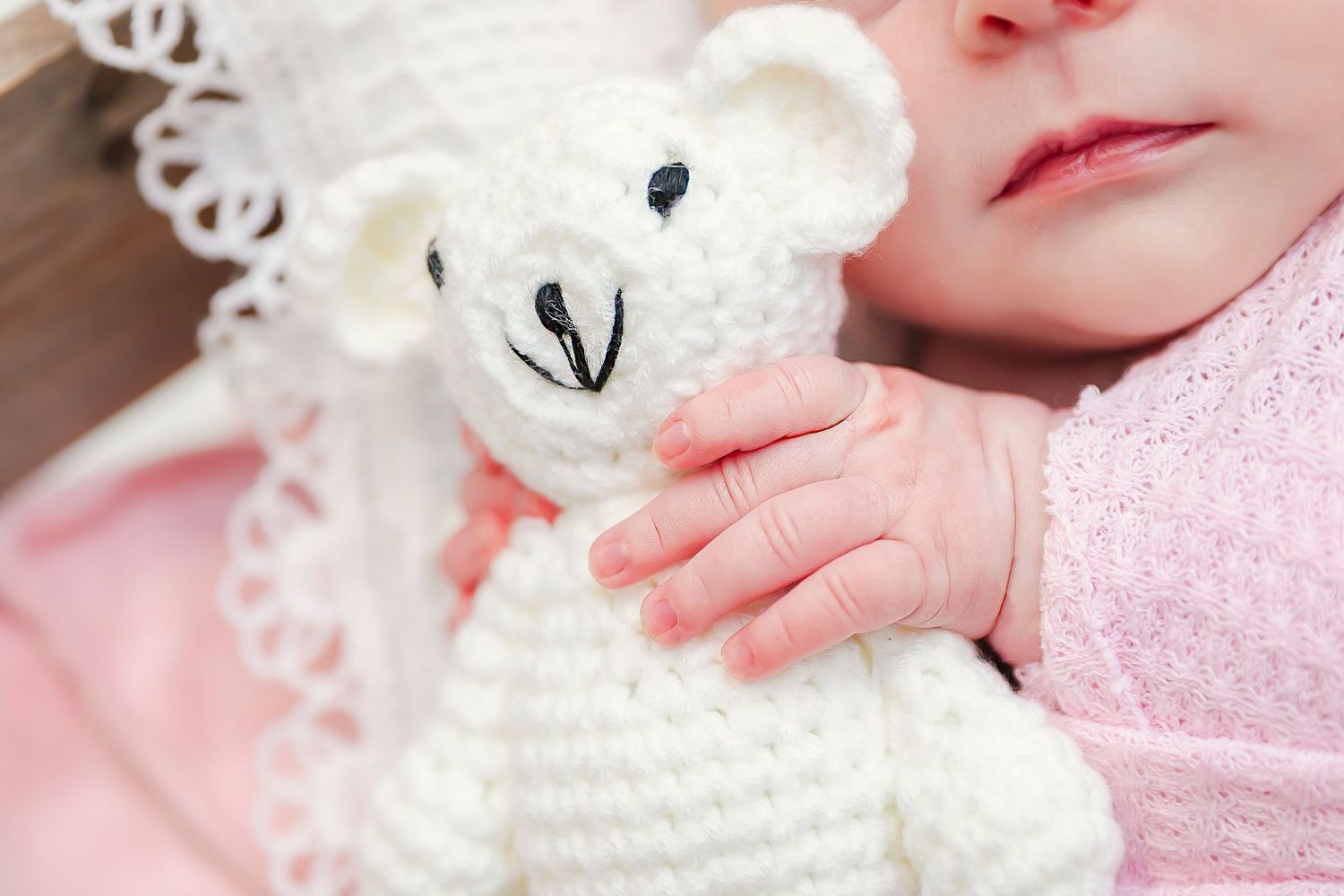 Newborn hand holds a white crocheted teddy bear creating a soft, delicate scene taken for newborn photography in Pittsburg Ks and Joplin Mo.